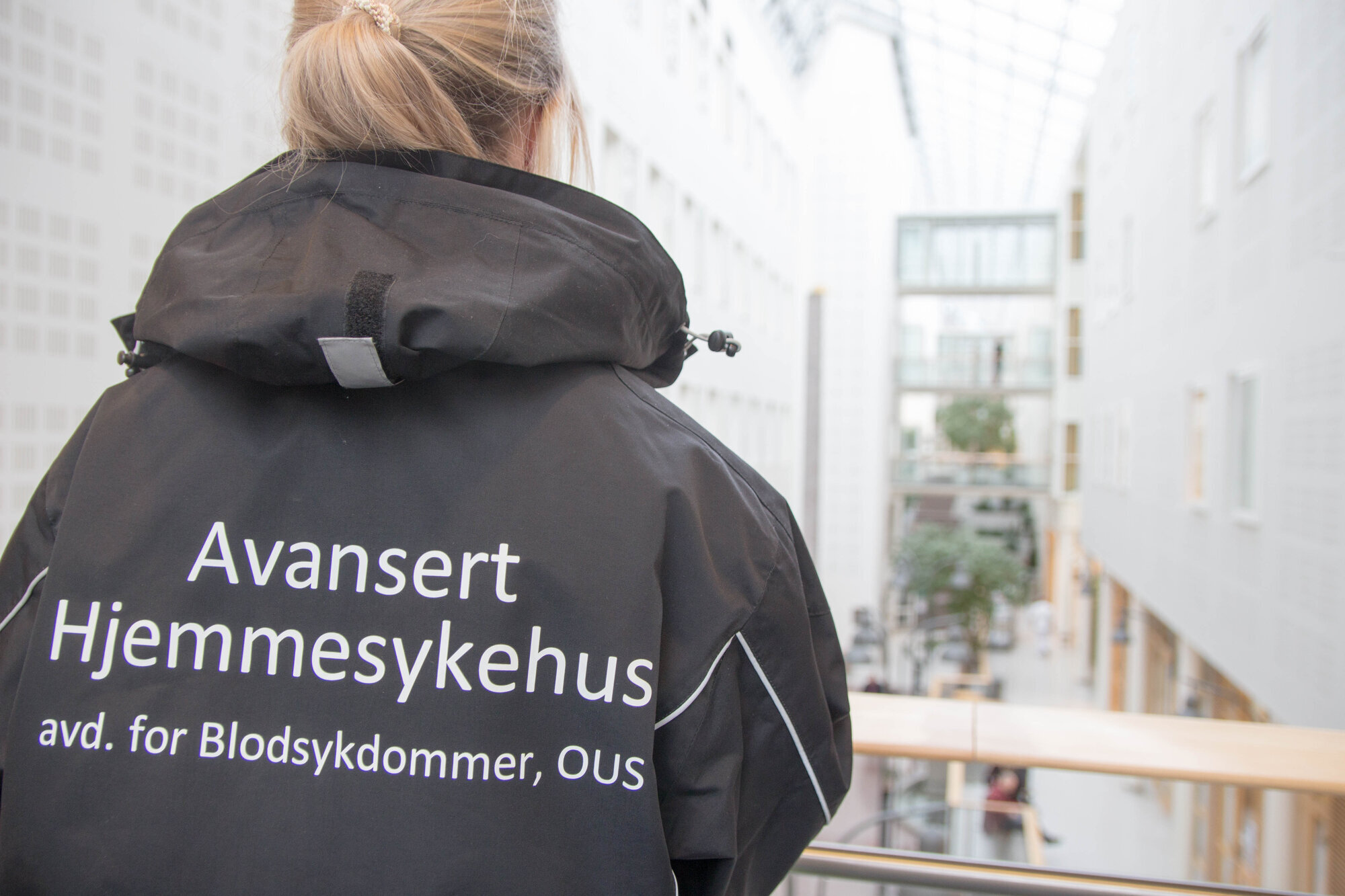 Avansert hjemmesykehus, Oslo universitetssykehus Bildet viser en sykepleier bakfra med jakke det står avansert hjemmesykehus på.