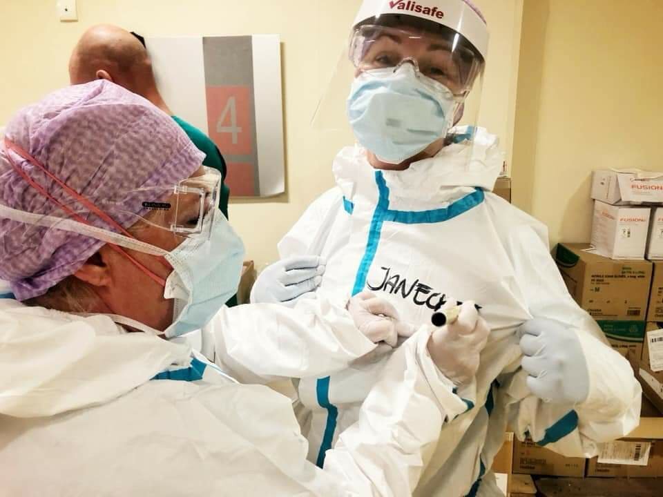 Medisinsk innsatsteam Bildet viser en sykepleier i smittevernutstyr som skriver navn på dressen til en annen sykepleier.