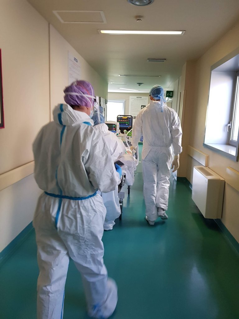 Medisinsk innsatsteam Bildet viser helsepersonell i smittevernutstyr som triller en seng med pasient.