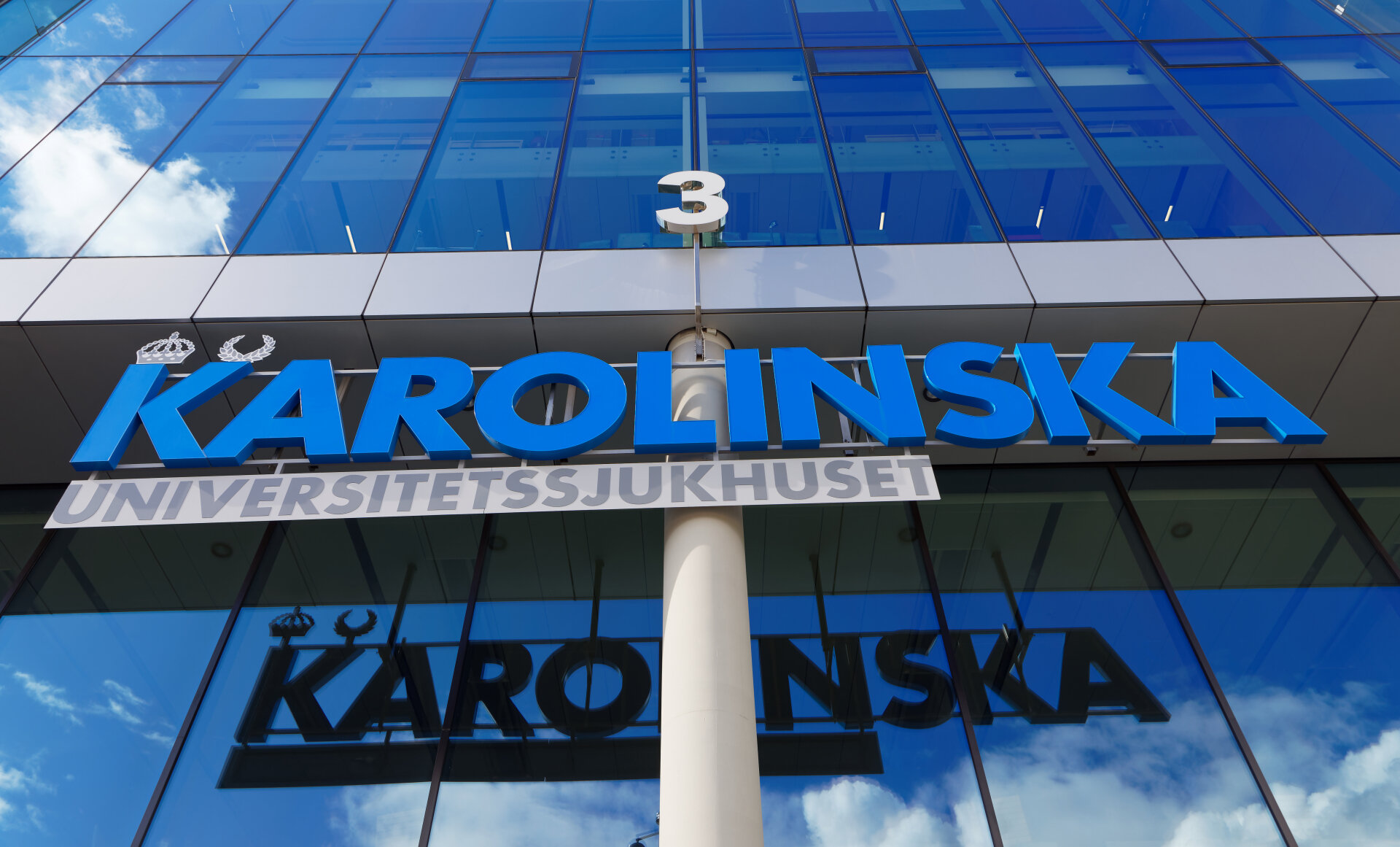 Karolinska universitetssjukhuset Bildet viser en bygning med et skilt der det står Karolinska i blå bokstaver.