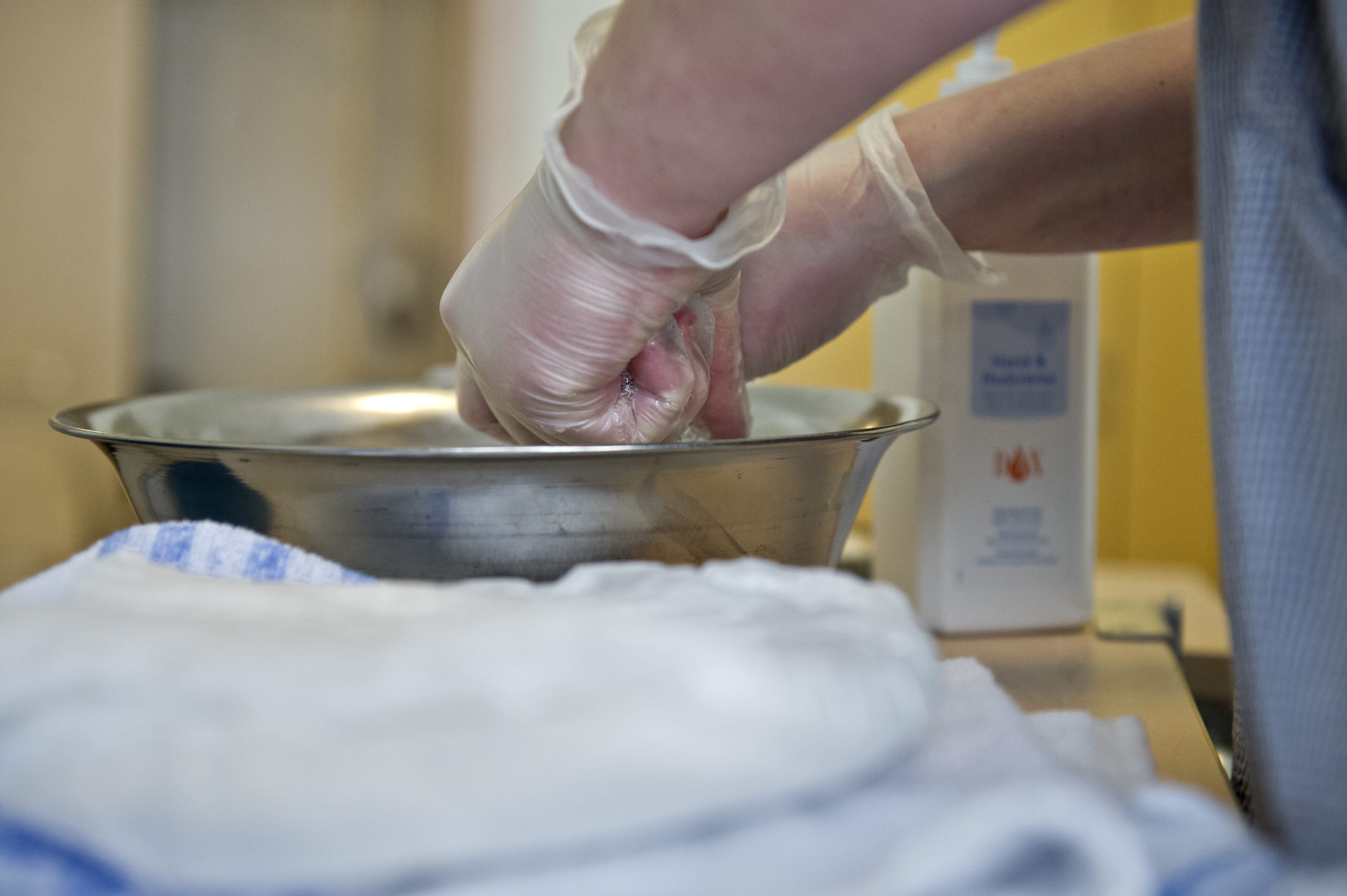 Bildet viser to hender med hansker som vrir opp en klut i et vaskevannsfat.