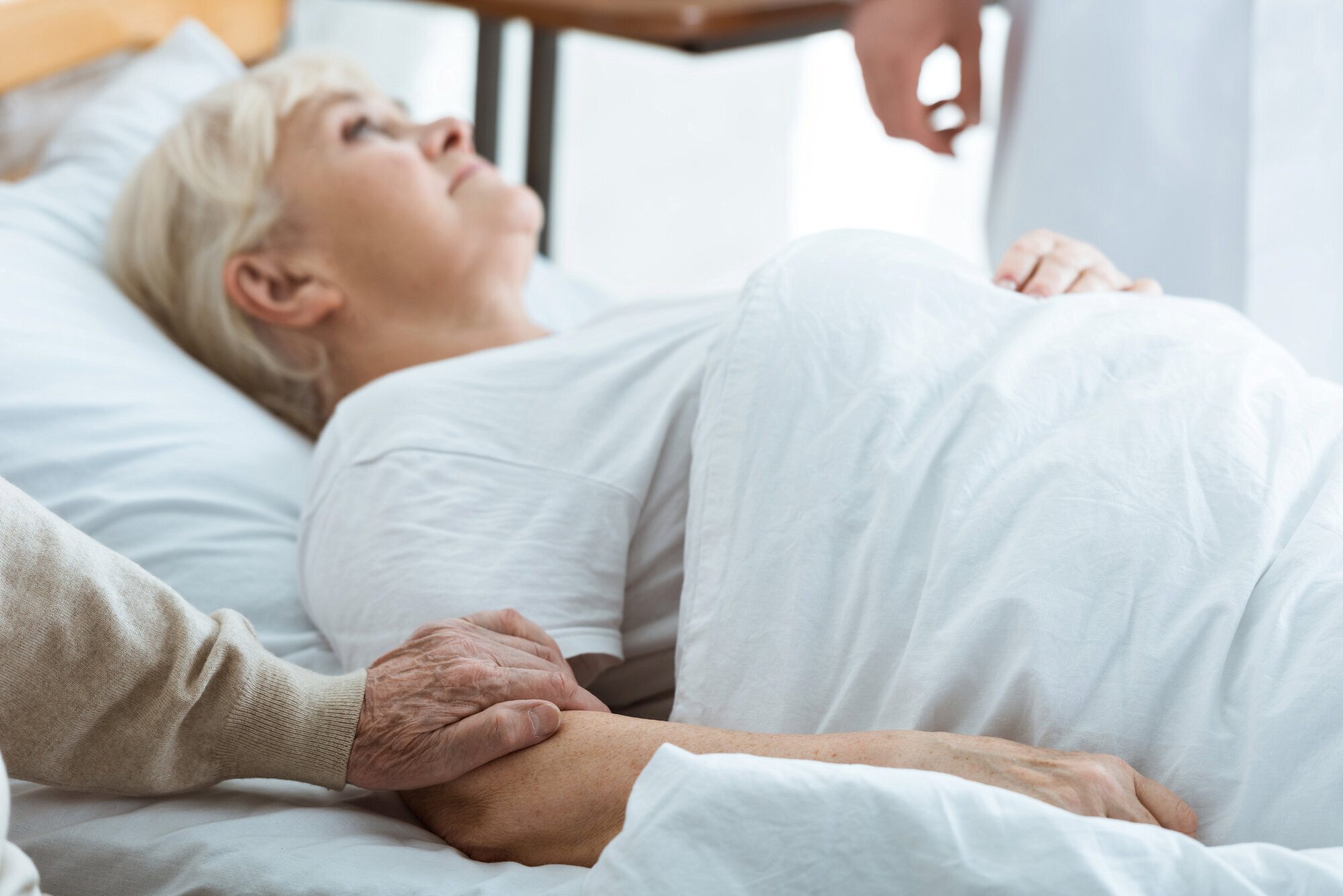Syk kvinne Bildet viser en eldre kvinne som ligger i en seng og en mann som holder henne i armen