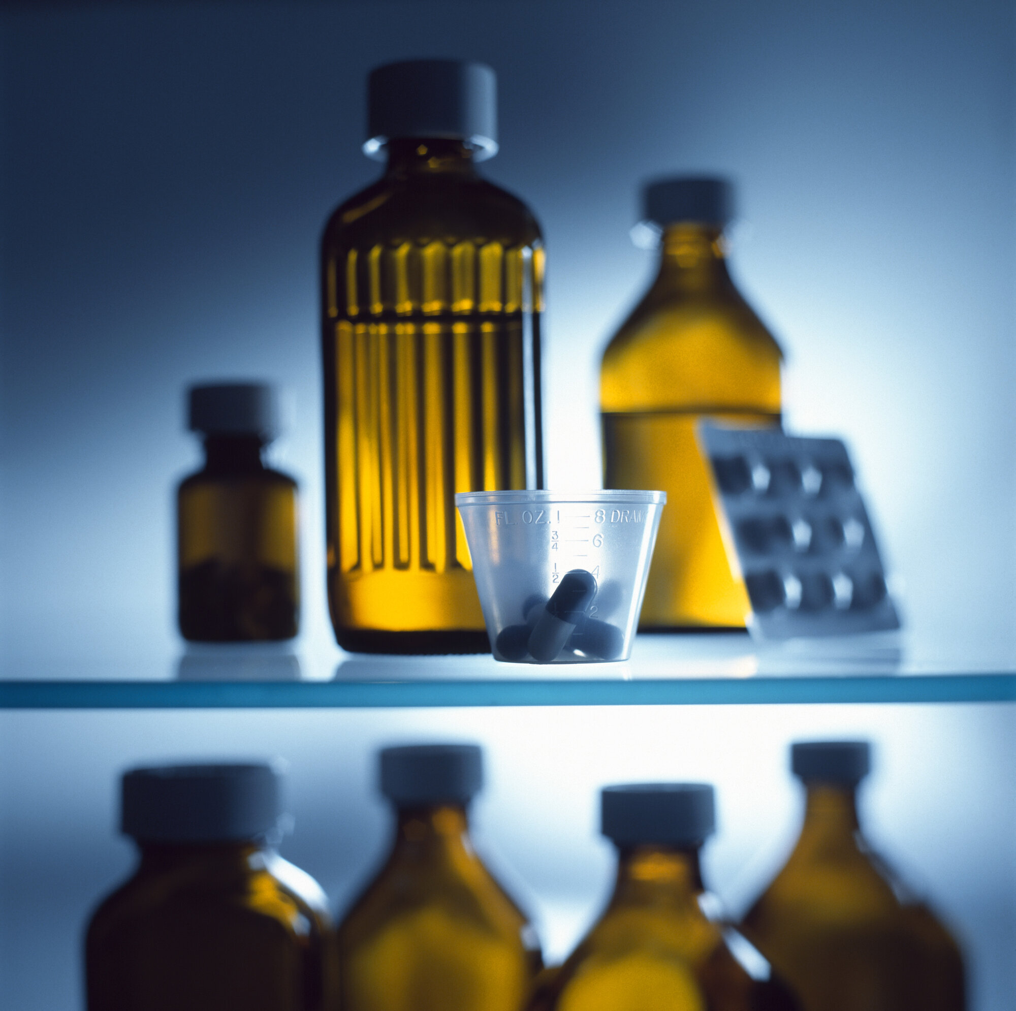 Medisiner, flasker, piller Bildet viser ulike flasker med legemidler, et brett med piller og et medisinbeger med piller.