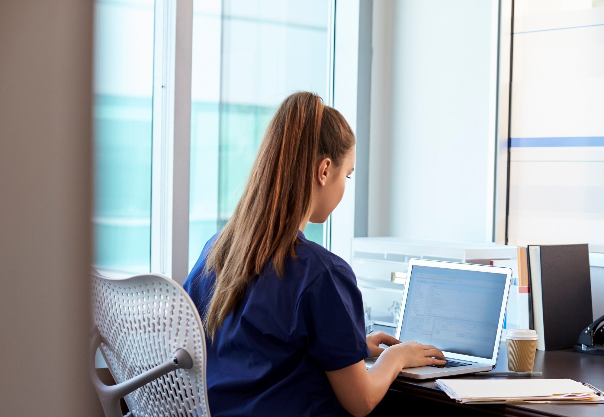 Sykepleier Bildet viser en sykepleier som sitter alene foran pc-en.