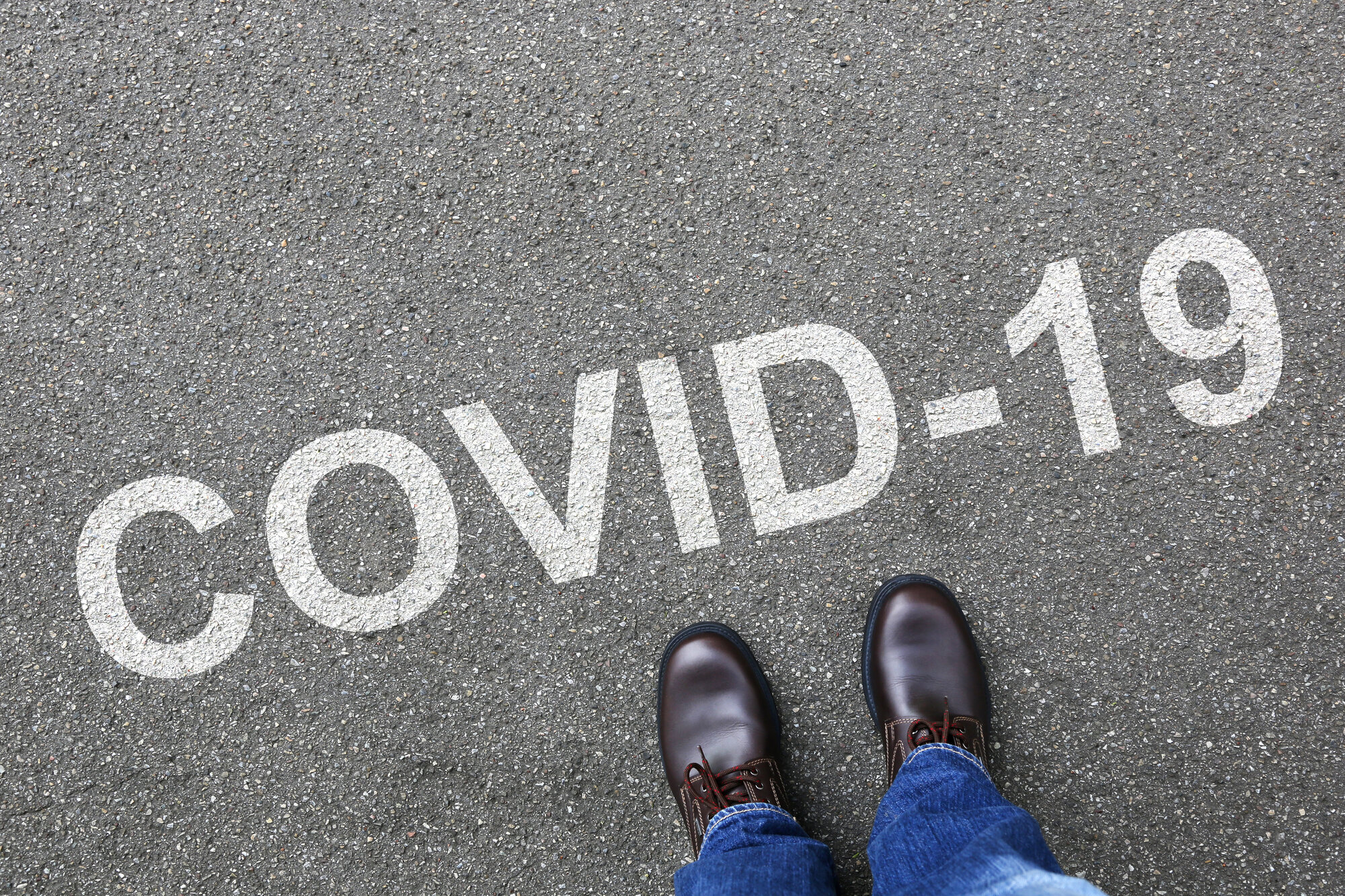 covid-19 Bildet viser et menneske som ser ned på bakken hvor det står covid-19