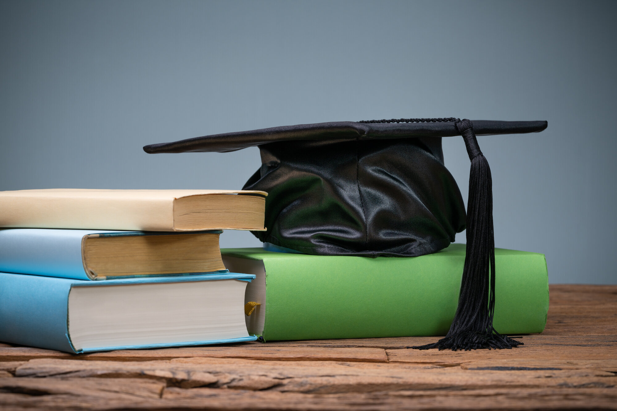 Studentlue og bøker Bildet viser en svart studentlue som ligger på en bokstabel på en gammel trepult