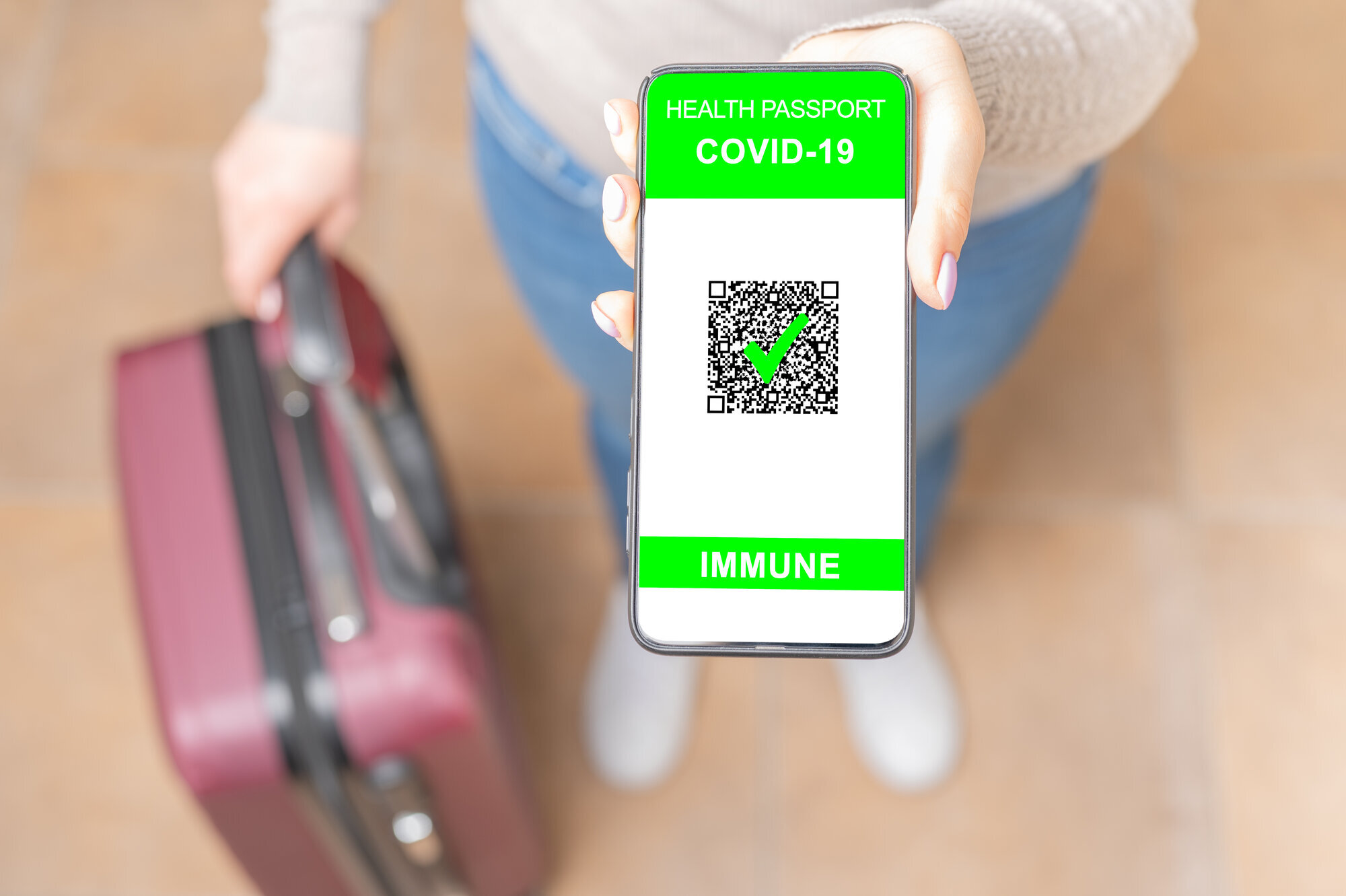 vaksine-pass Bildet viser en kvinne med en koffert som viser, med mobilen sin, at hun er vaksinert for covid-19