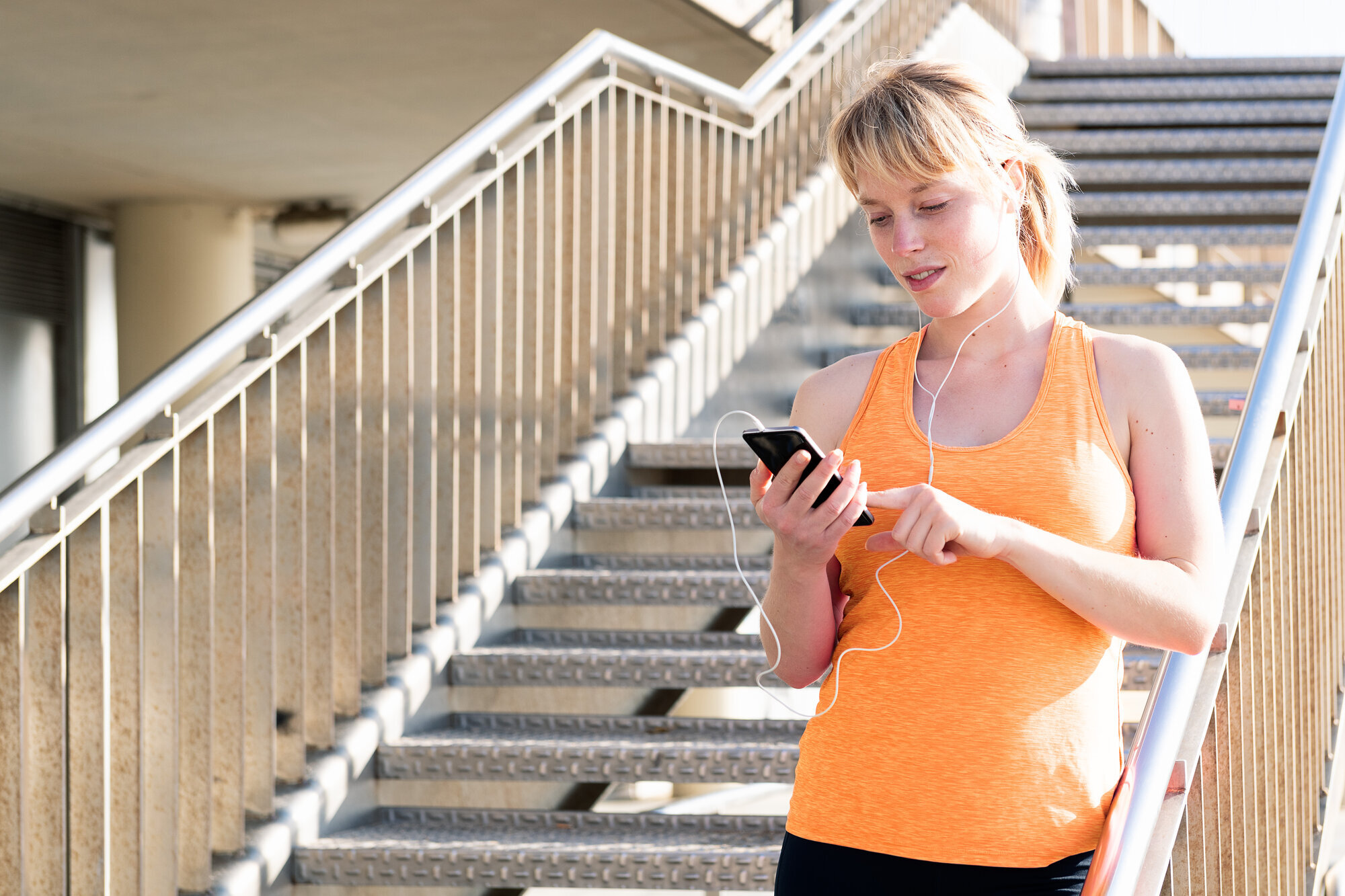 Kvinne ser på telefon Bildet viser en ung kvinne med høretelefoner som ser på en telefon