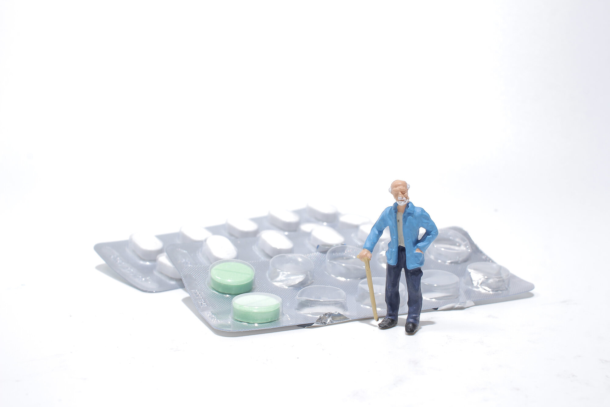 Sykepleiermangel Bildet viser en figur av en eldre mann som står ved siden av et brett med medisiner