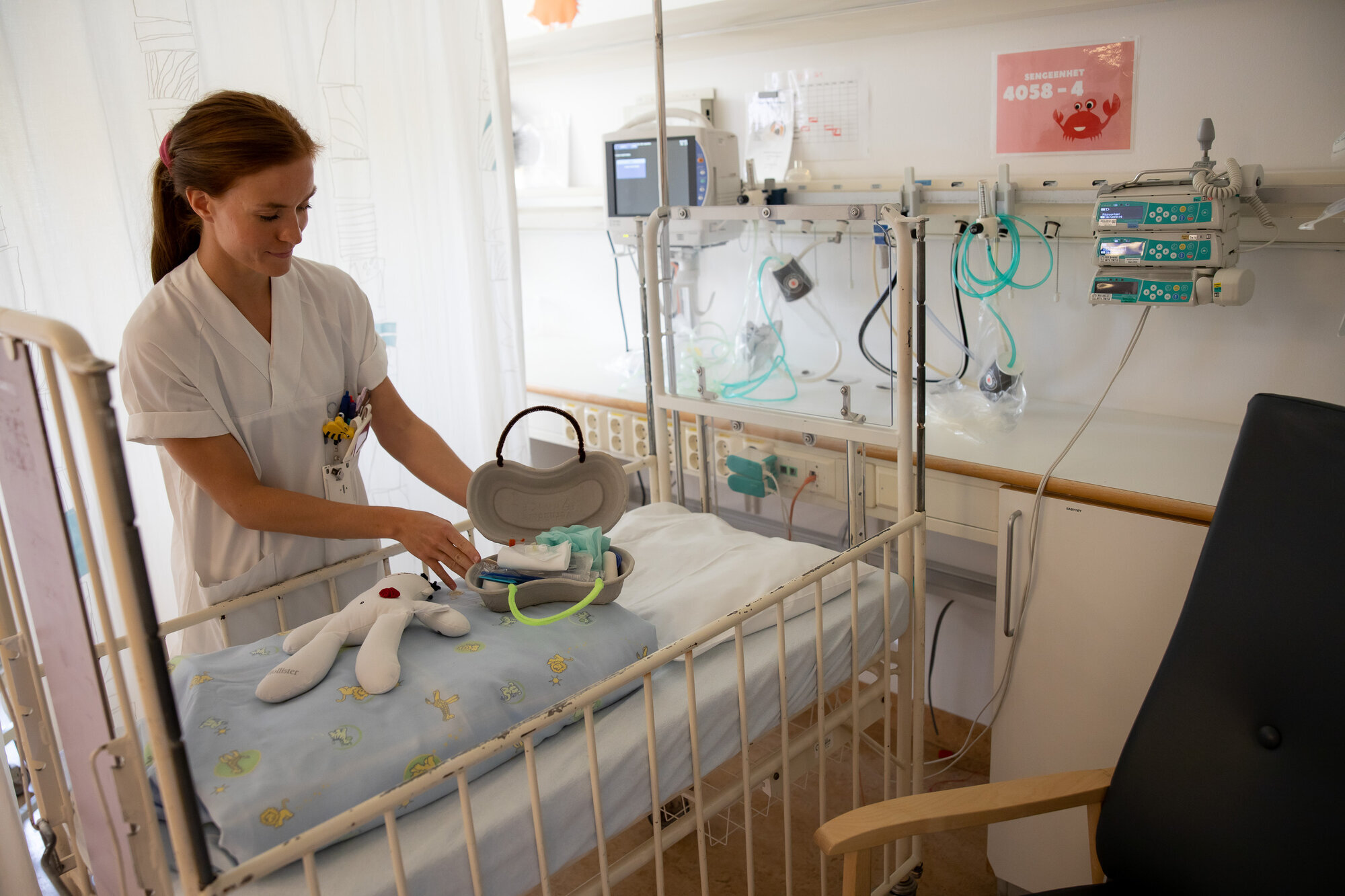Sykepleier, barneavdeling Bildet viser en sykepleier som legger frem en dukke og et førstehjelpsskrin laget av pussbekken.