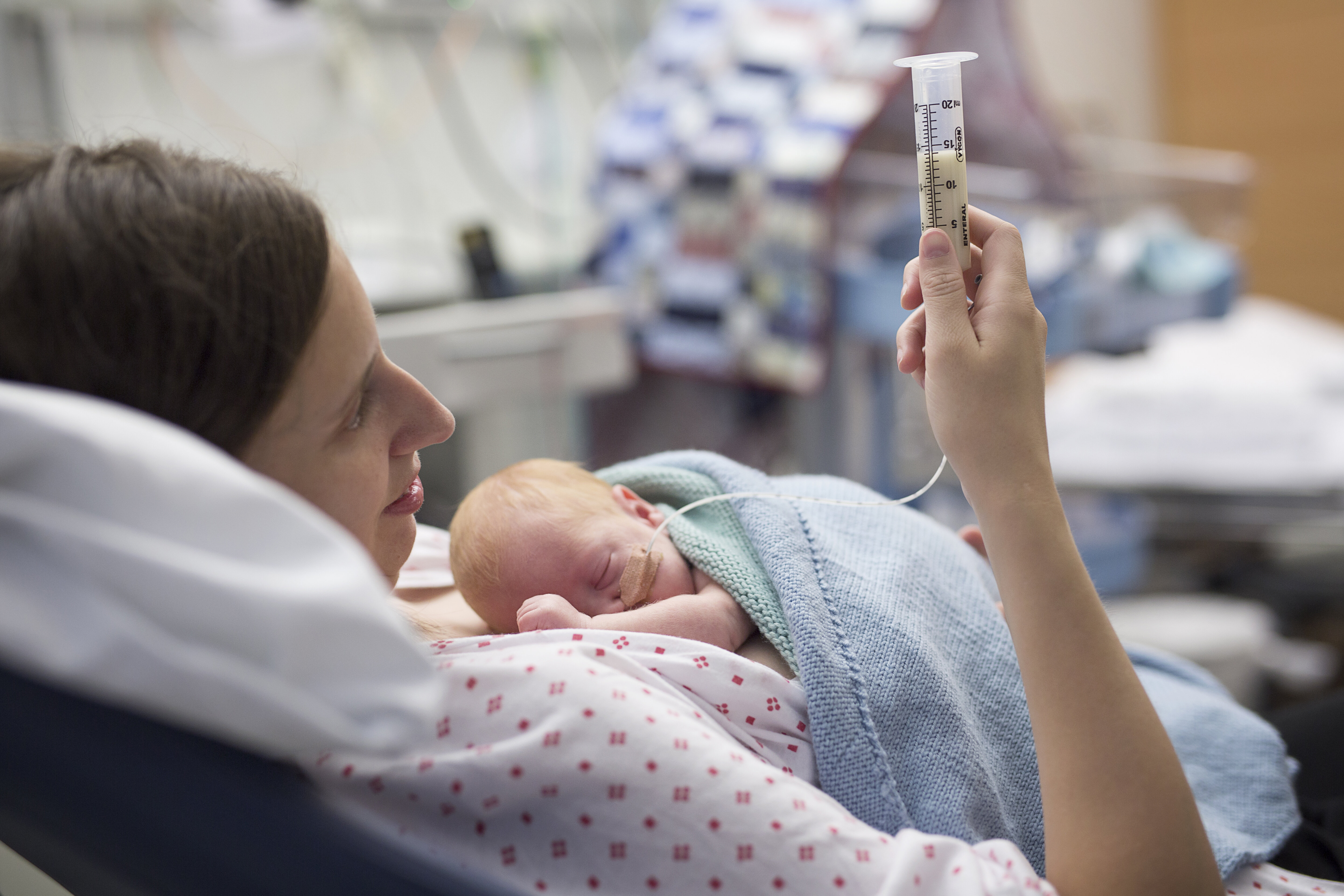 Nyfødt baby og mor på familierom Bildet viser en kvinne på nyfødtintensiven. Hun ligger i sengen og mater sin nyfødte baby ved hjelp av sonde