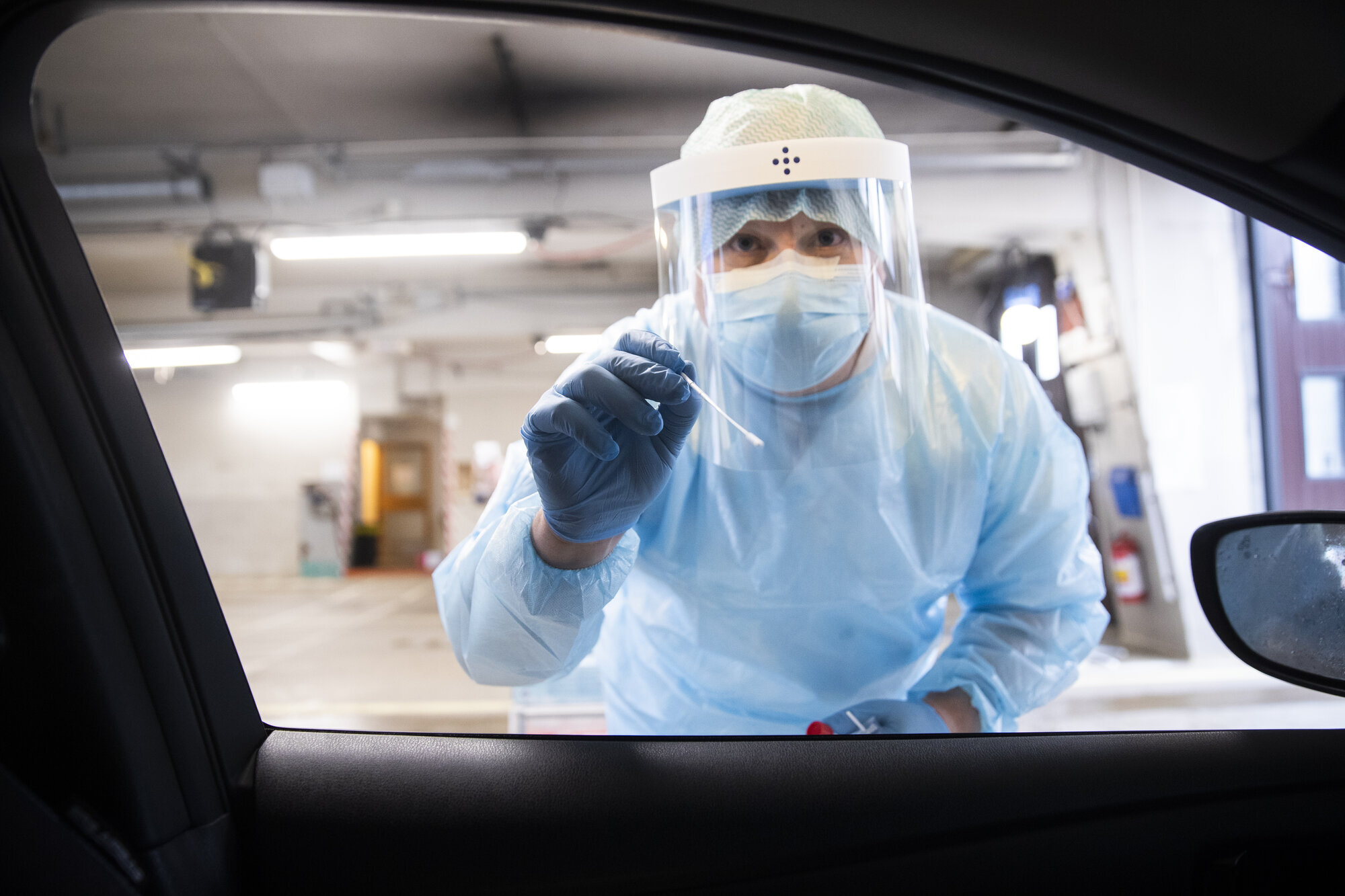Helsearbeider, koronatest Bildet viser en helsearbeider i smittevernutstyr som holder frem en testpinne.