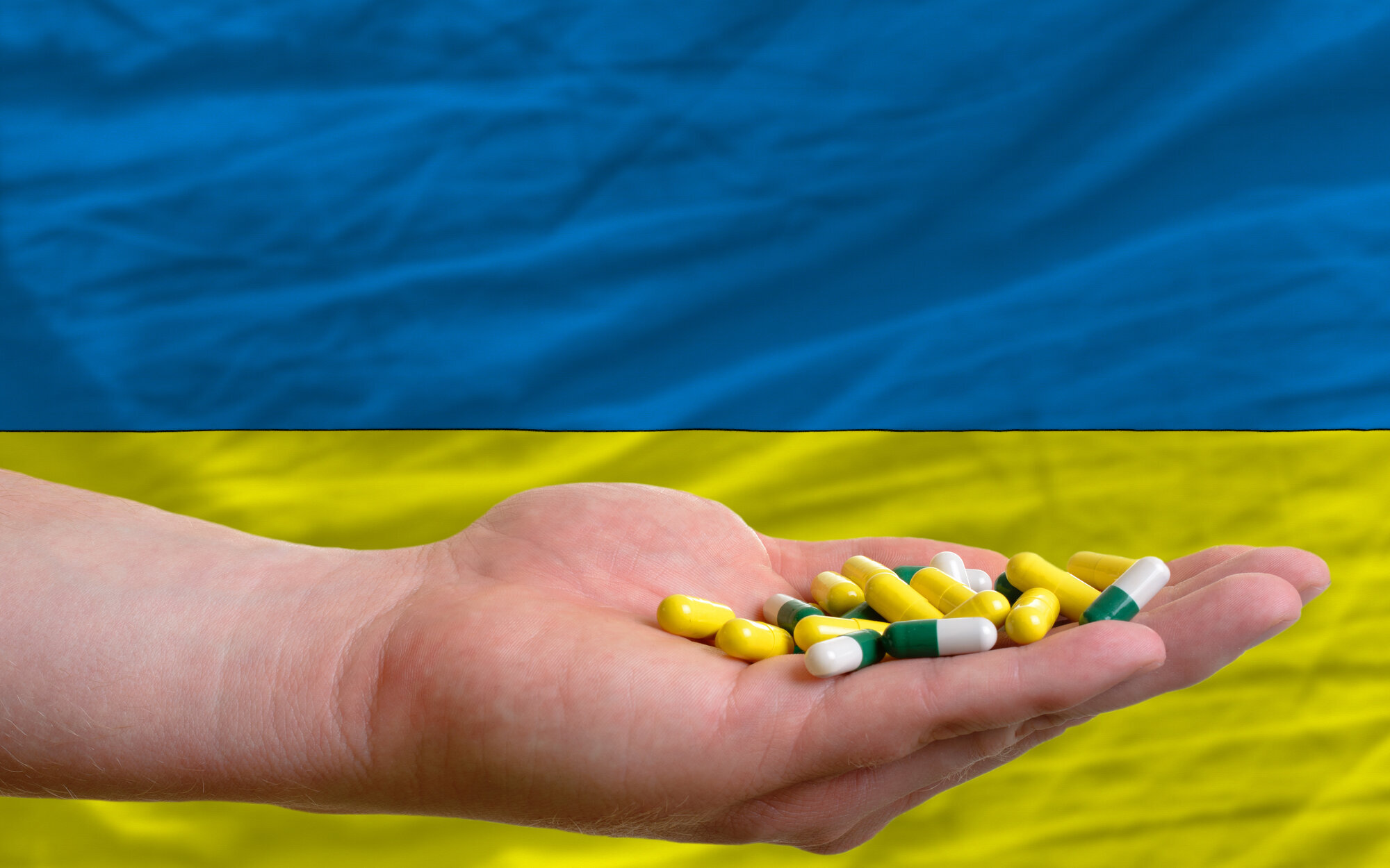 Medisiner, Ukraina Bildet viser en hånd som holder piller, i bakgrunnen ses litt av det ukrainske flagget.
