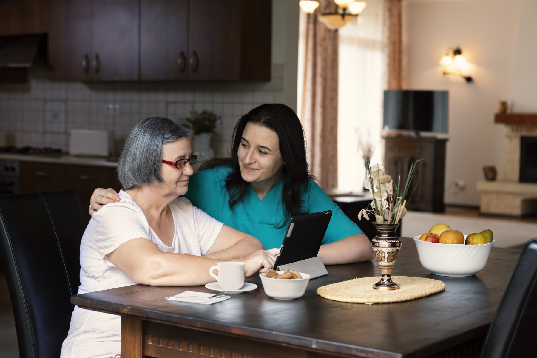 Omsorg Bildet viser et helsepersonell som holder rundt en eldre kvinne som ser på et nettbrett