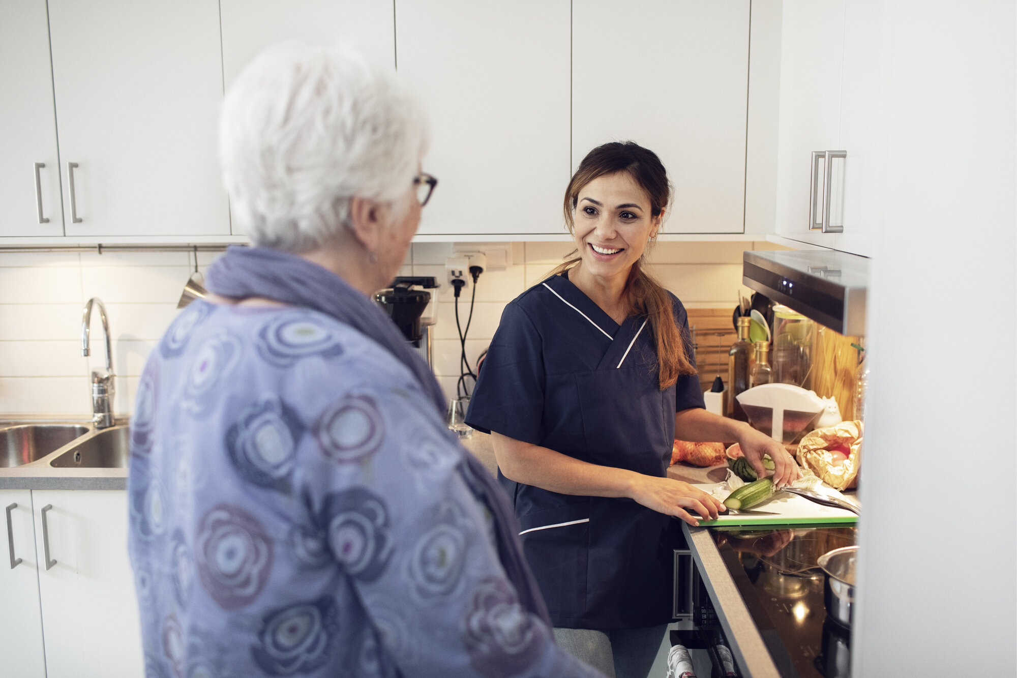 Sykepleier og pasient Bildet viser en kvinnelig sykepleier som smiler og snakker med en eldre kvinne