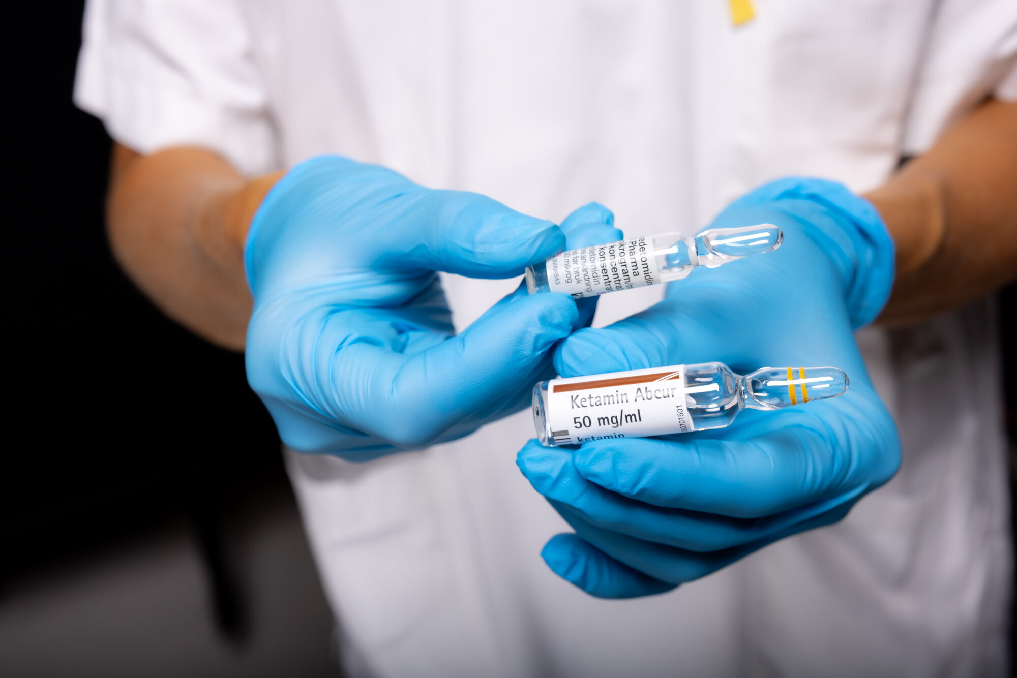 Legemidler for nasal smertelindring Bildet viser to hender med blå hansker som holder to ampuller med legemidlene deksmedetomidin og ketamin