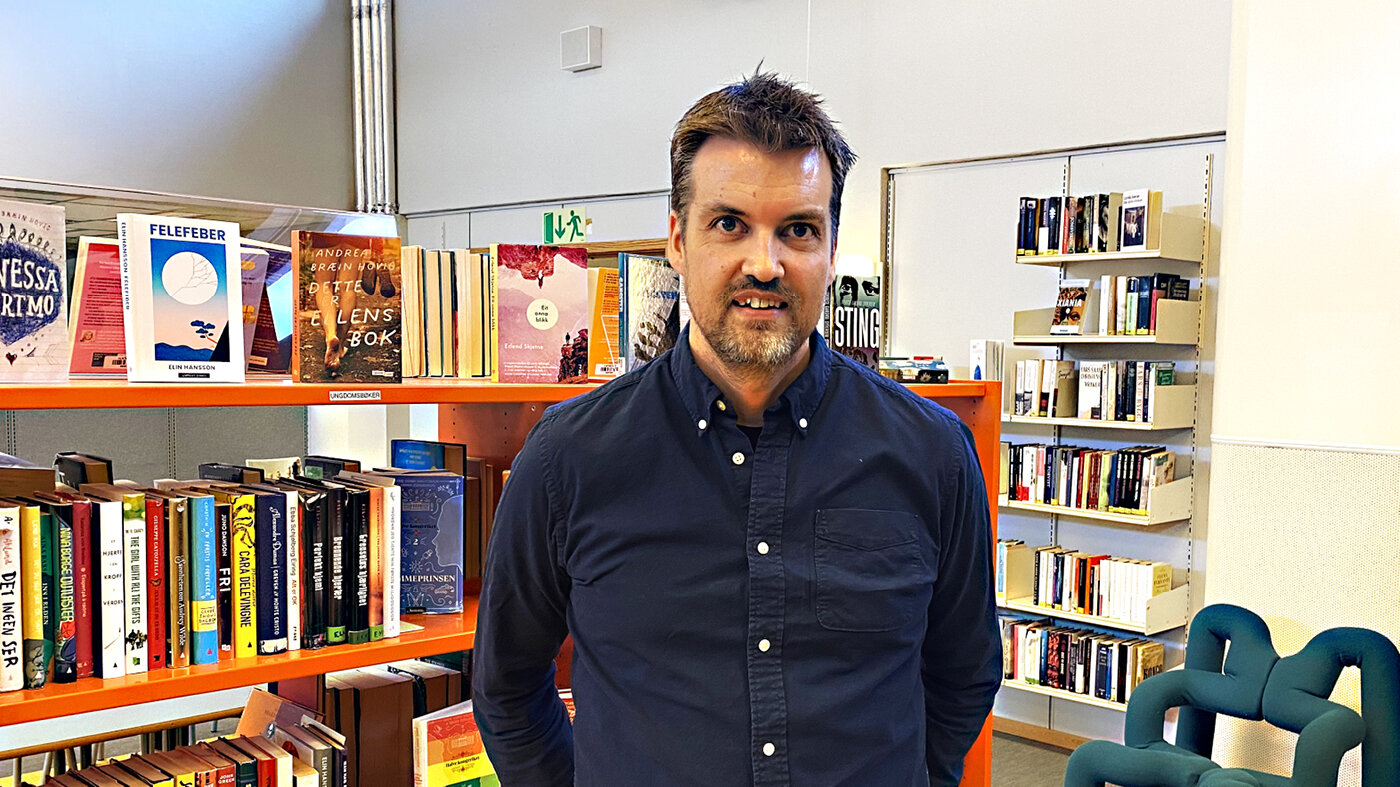 Bildet viser innleggsforfatteren foran hyller med barnebøker på et bibliotek..