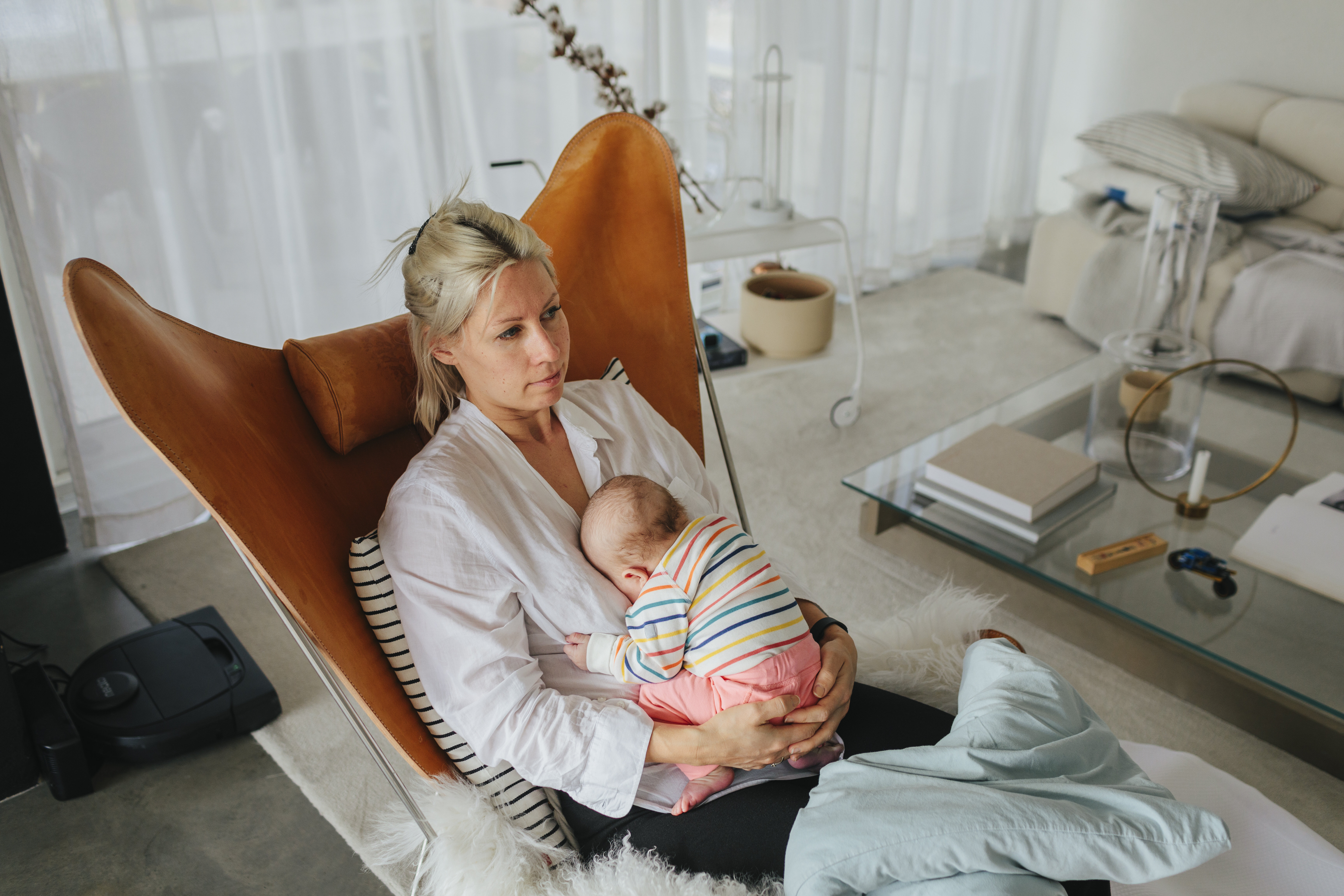 Mother with newborn baby The photo shows a young mother sitting in a chair in her living room. She looks tired and holds her newborn baby in her lap.