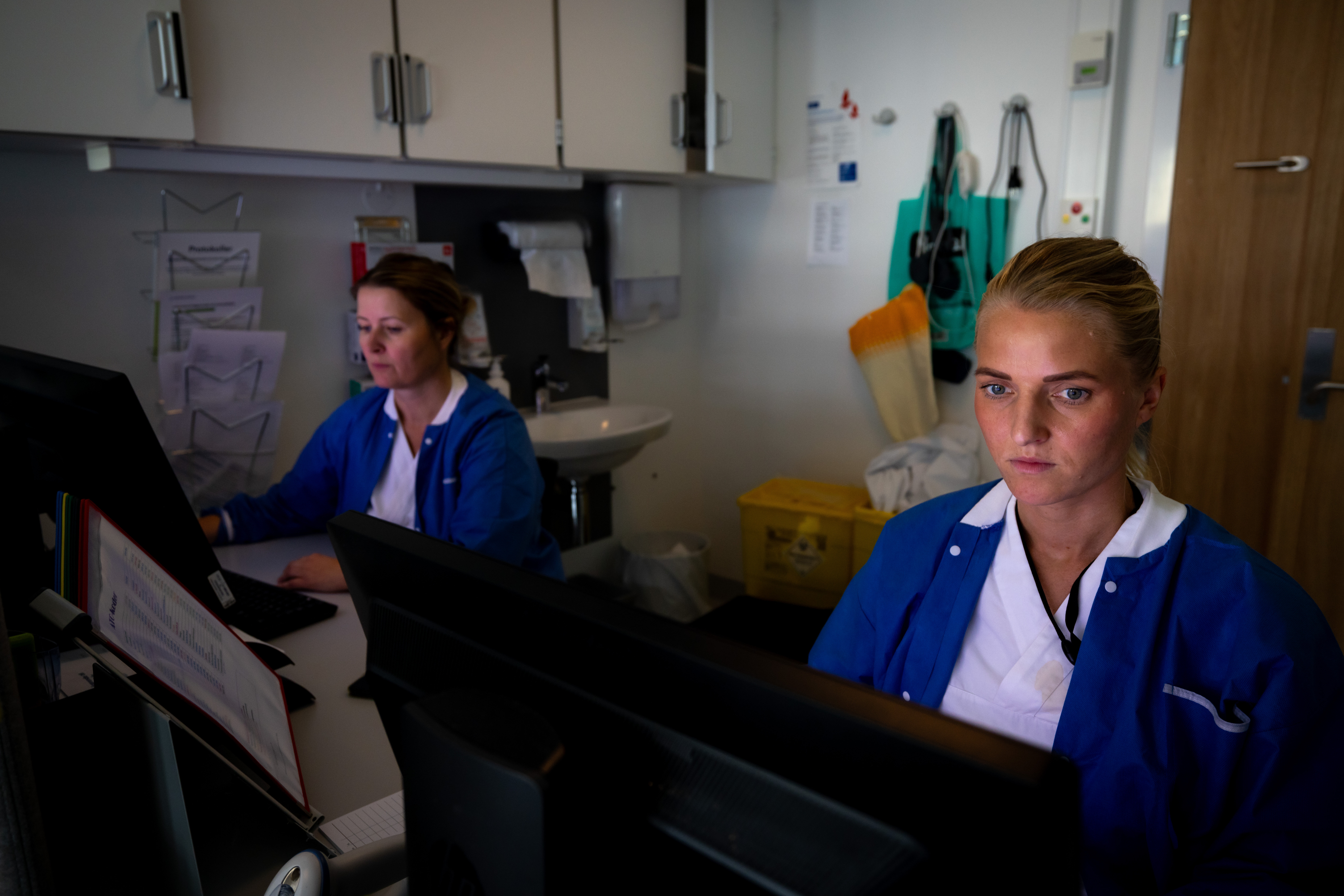 The photo shows two nurses in front of a computer each.