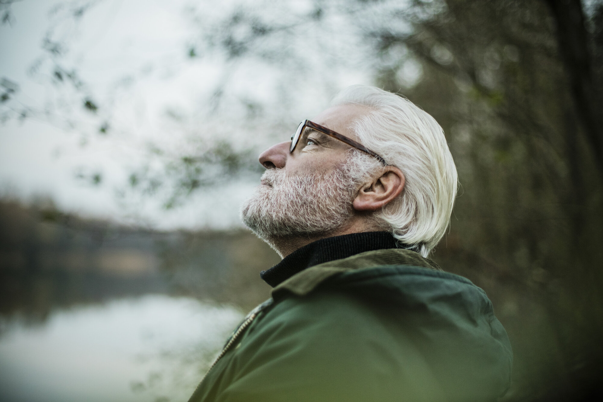 Bildet viser en eldre mann som ser tankefullt ut i luften ved et vann