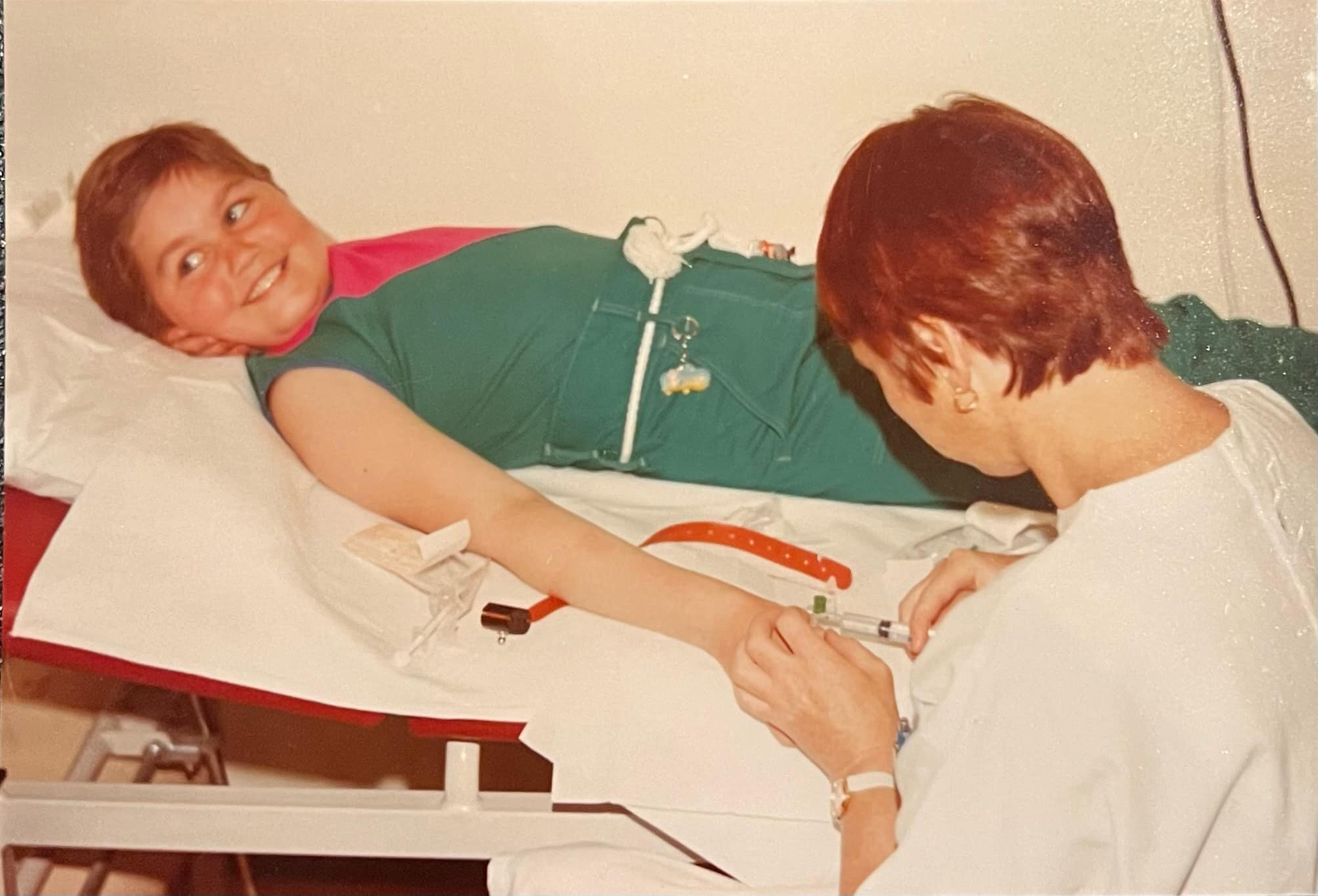 Privat barn i grønne klær blir behandlet av en sykepleier. Barnet ligger på rygg i en seng