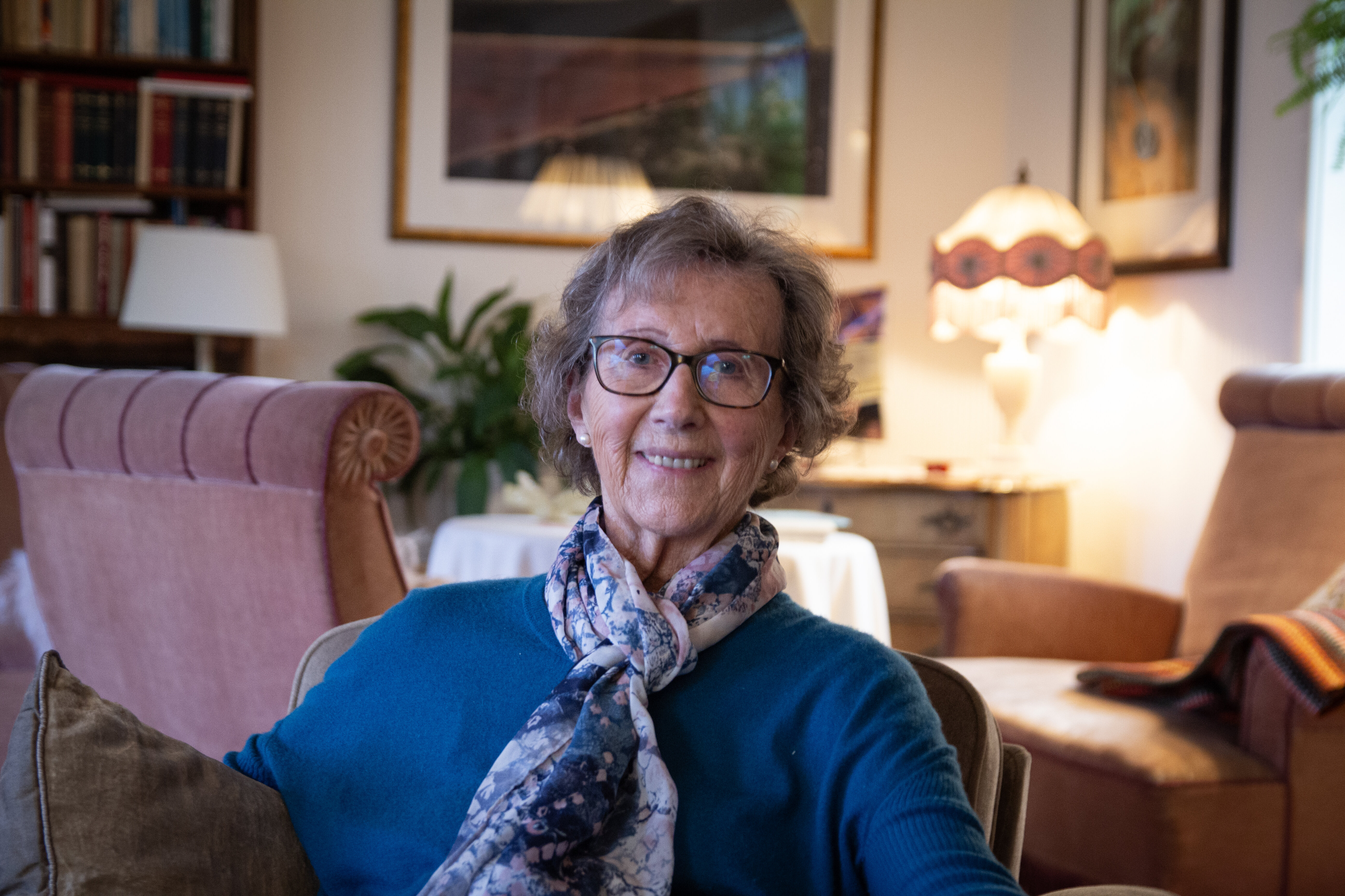 Signy Romslo sitter hjemme i soffa og siler til kamera