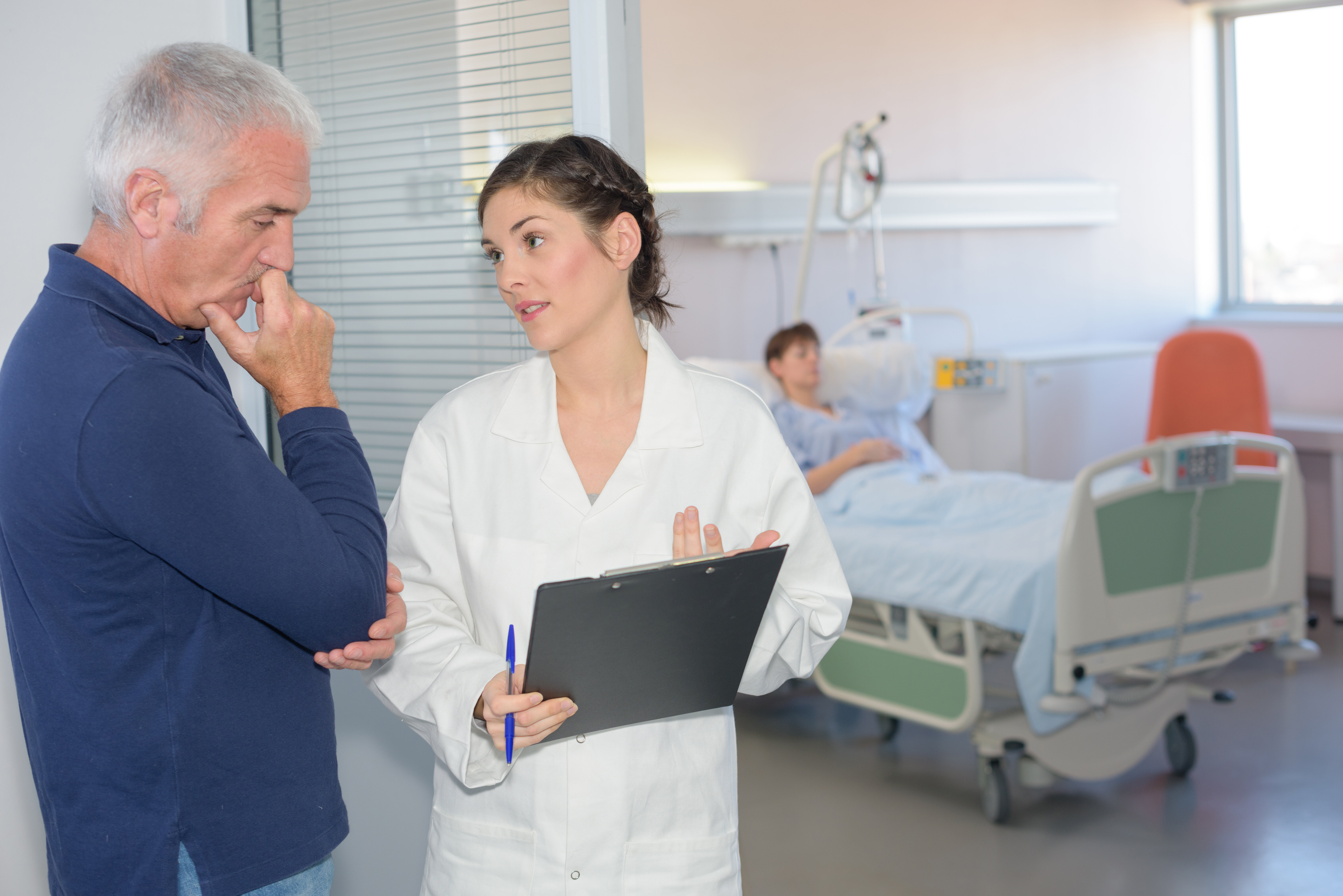 Bilde viser pårørende i samtale med helsepersonell. Pasient ligger i en seng i bakgrunn.