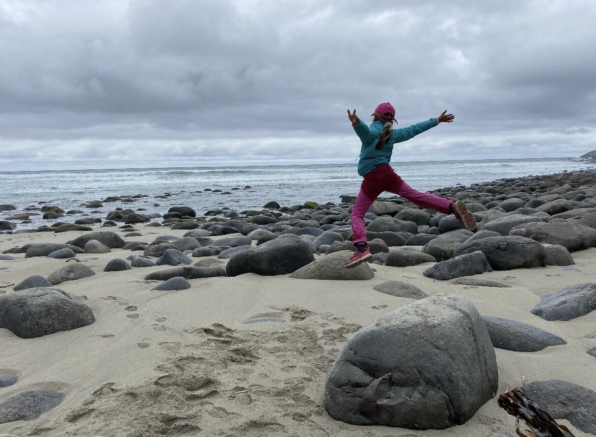 Bildet viser et barn som hopper fra stein til stein på en strand