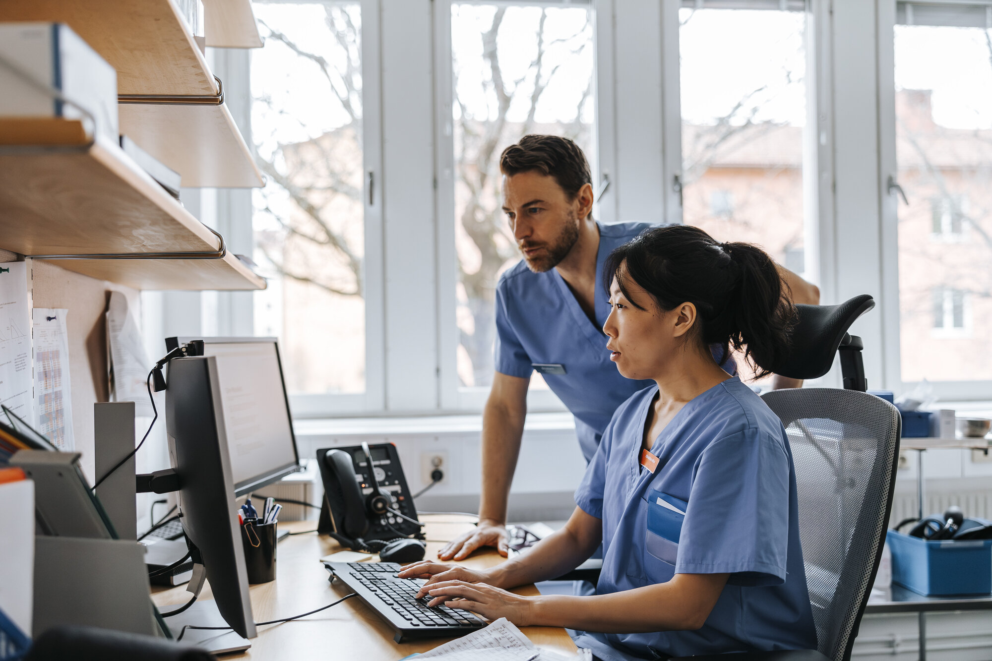 Bildet viser to sykepleiere som har overlevering av informasjon på vaktrommet