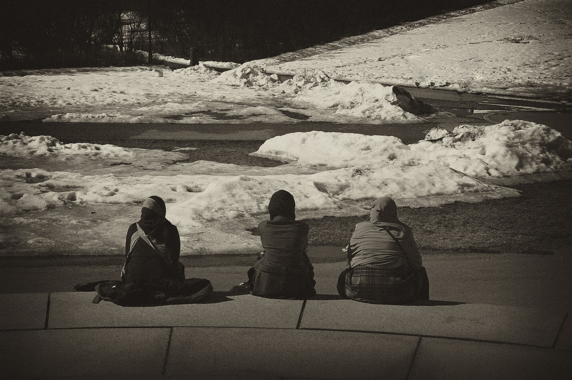 Bildet i sort og hvitt viser tre innvadrerkvinner bakfra som sitter på en steintrapp. Det er avstand mellom dem og de ser utover landskapet.