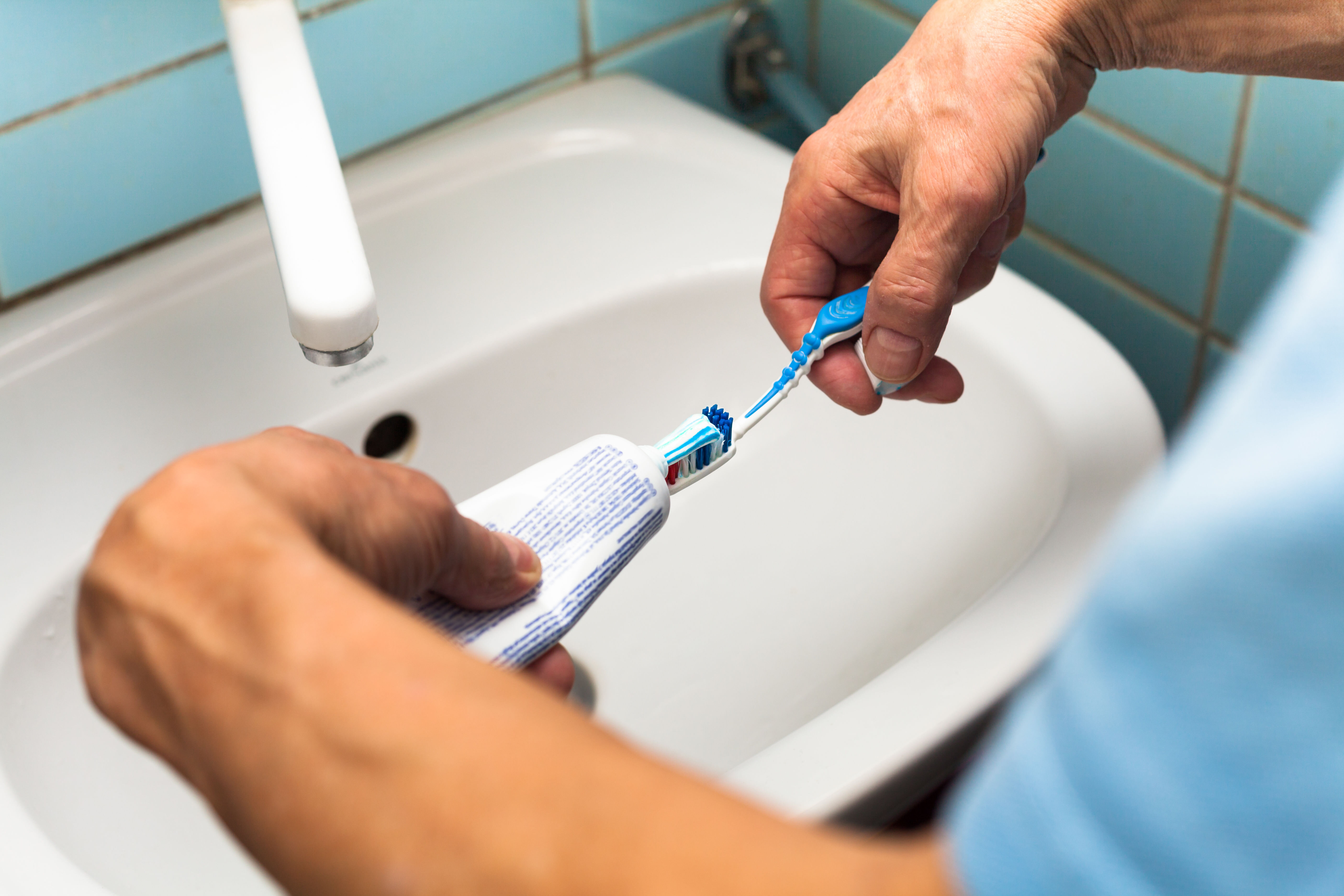 Munnhygiene, munnstell Bildet viser to hender som tar tannkrem på en tannbørste.