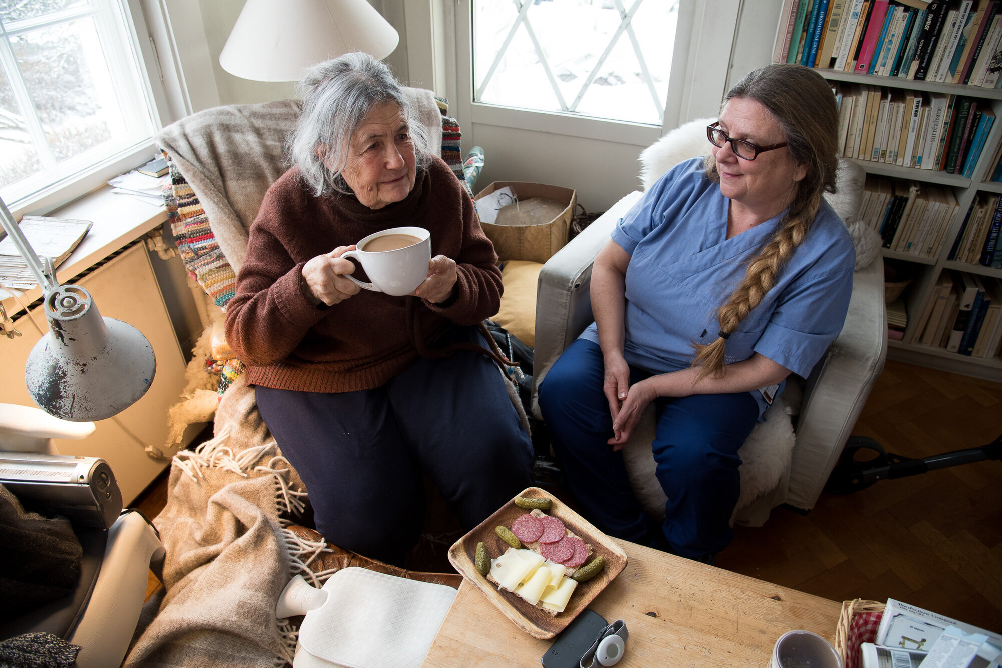 Måltid servert til beboer av hjemmesykepleieren Bildet viser en beboer som drikker kaffe sammen med hjemmesykepleieren. Foran beboeren står et fat med påsmurte brødskiver.