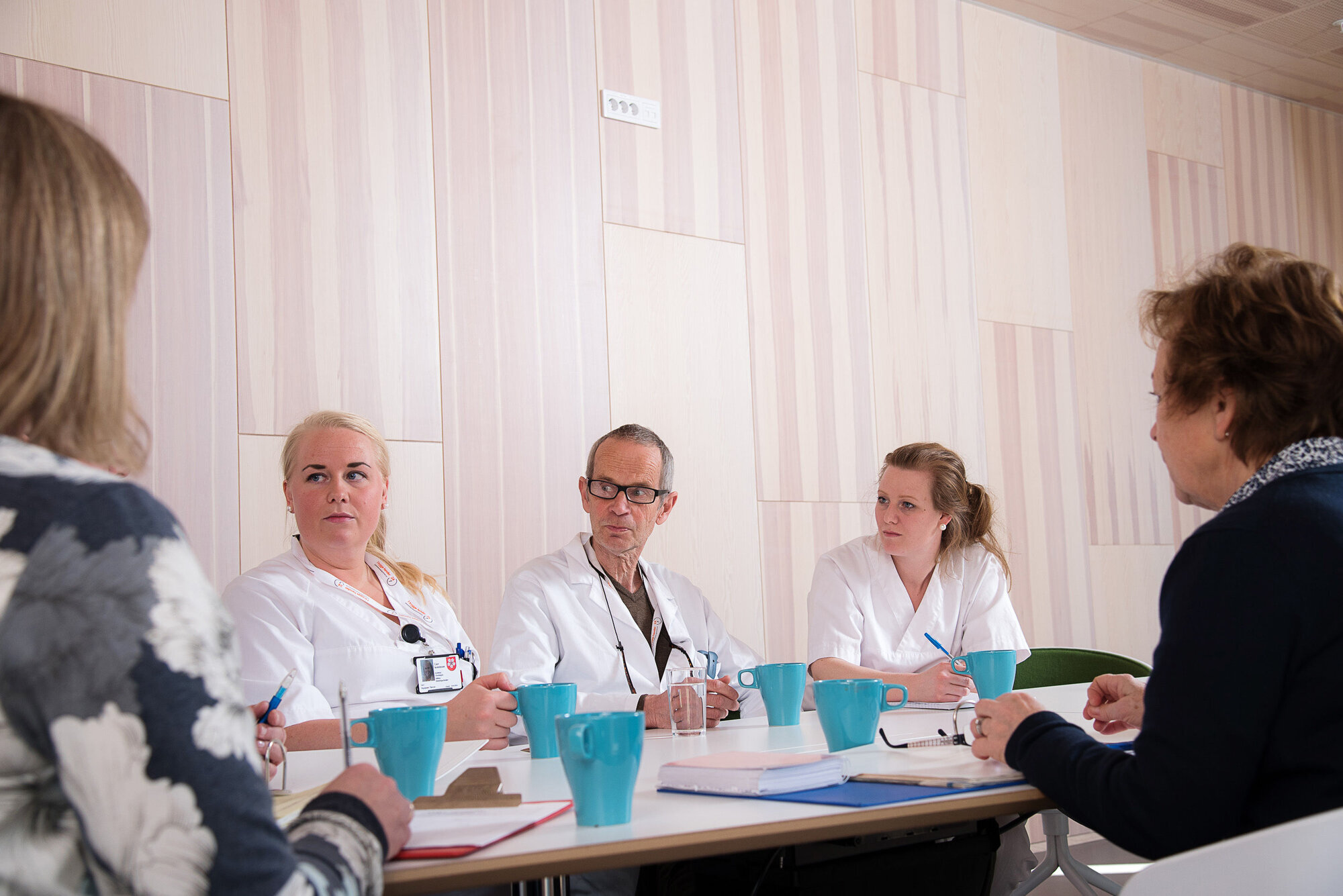 Helsepersonell på pauserommet Bildet viser helsepersonell som sitter rundt et bord. Noen har uniform, andre ikke.