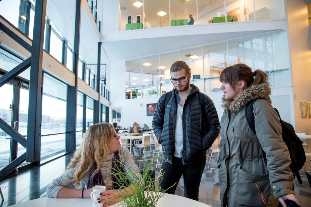 Bildet viser Anette Sagen som sitter ved et bord i kantinen og snakker med to medstudenter som st&aring;r.