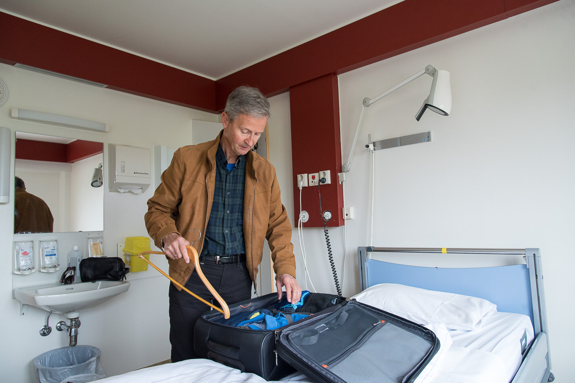 Bildet viser en mann som pakker ut kofferten sin på en seng på rommet på sykehuset Innleggelse på sykehus