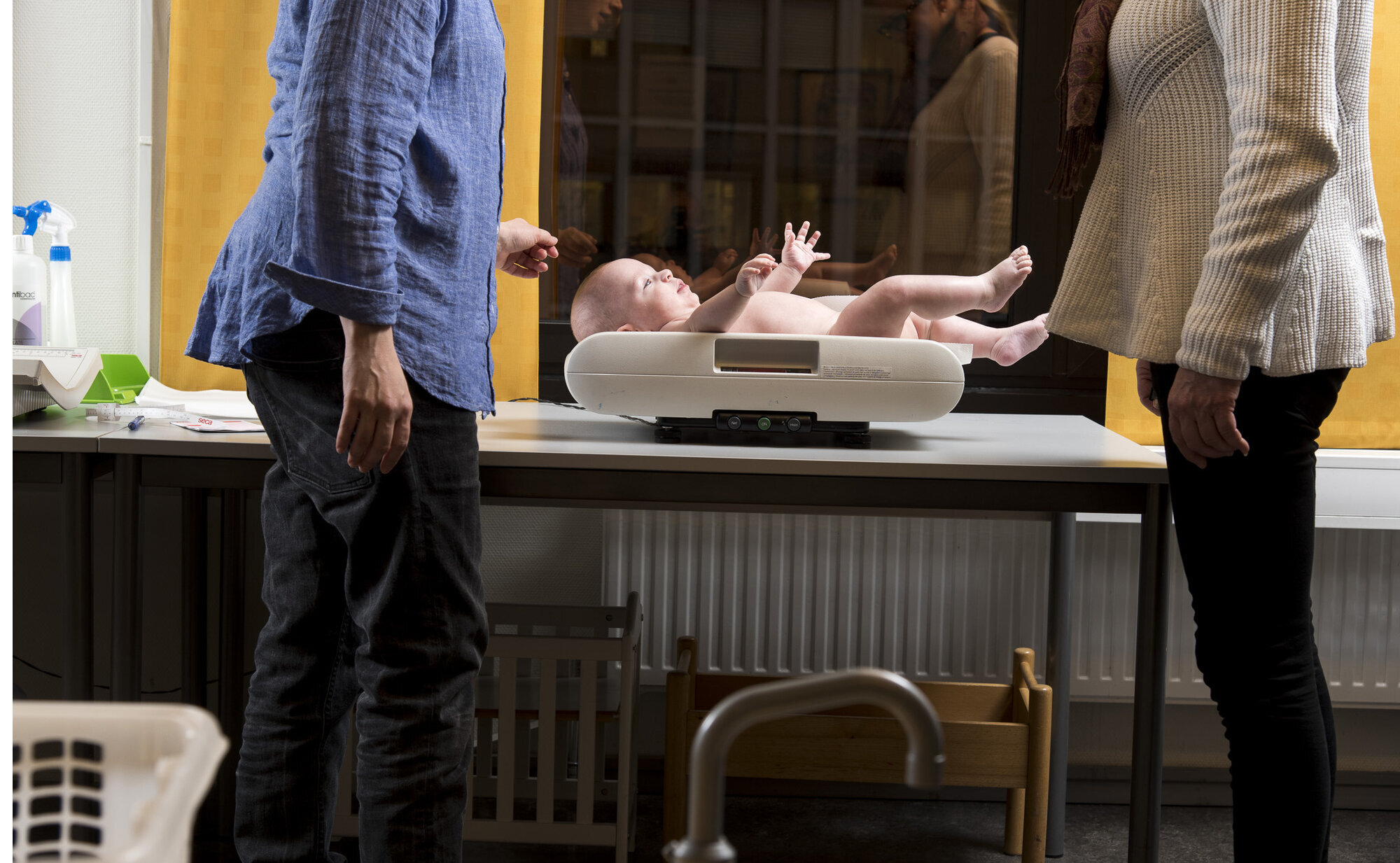 Veiing av baby på helsestasjonen Bildet viser en mor som er på helsestasjonen, der babyen veies av helsesøster.