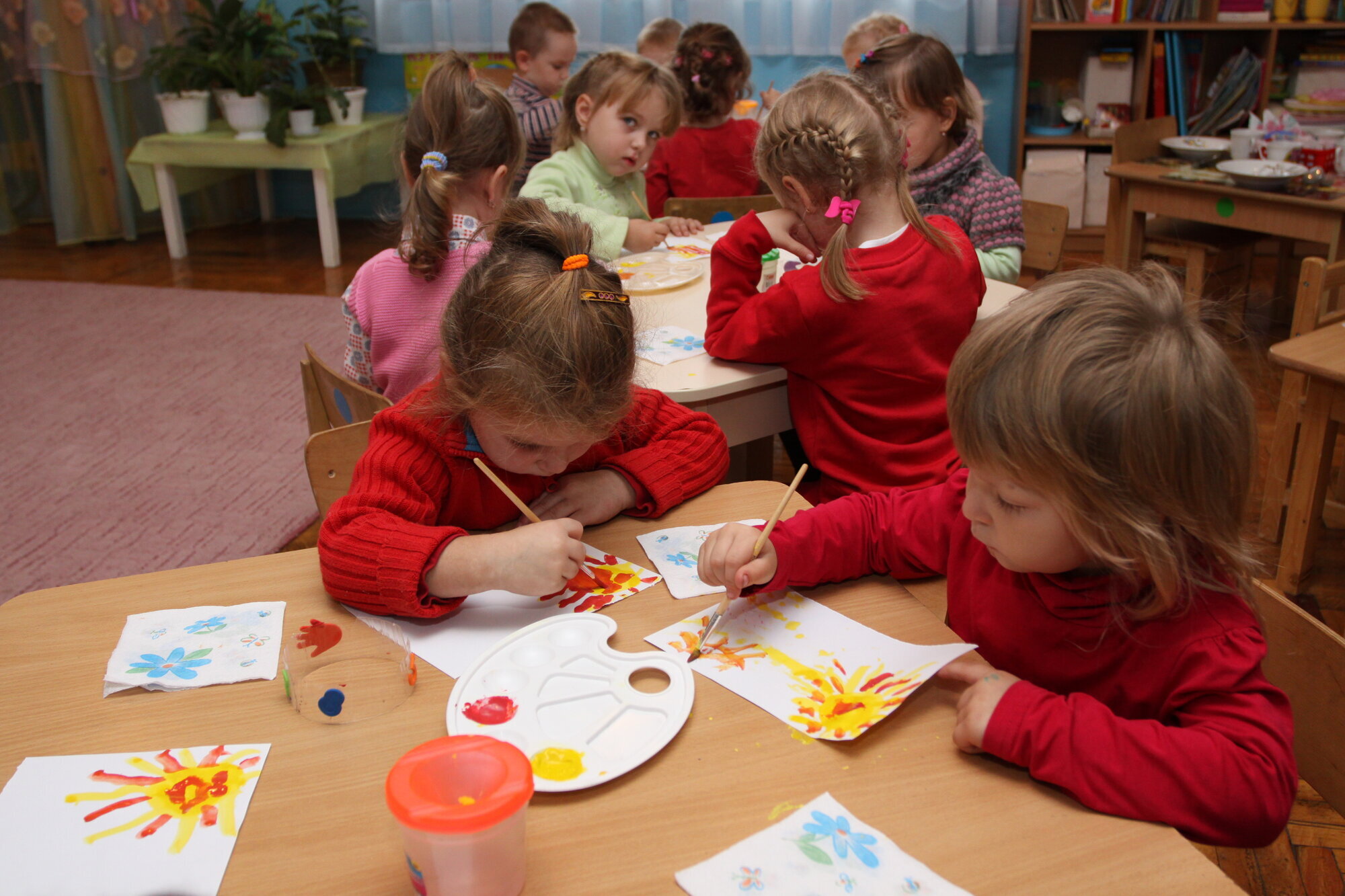 Barn i en barnehage som sitter rundt små border og tegner. Barn i en barnehage som sitter rundt små border og tegner.