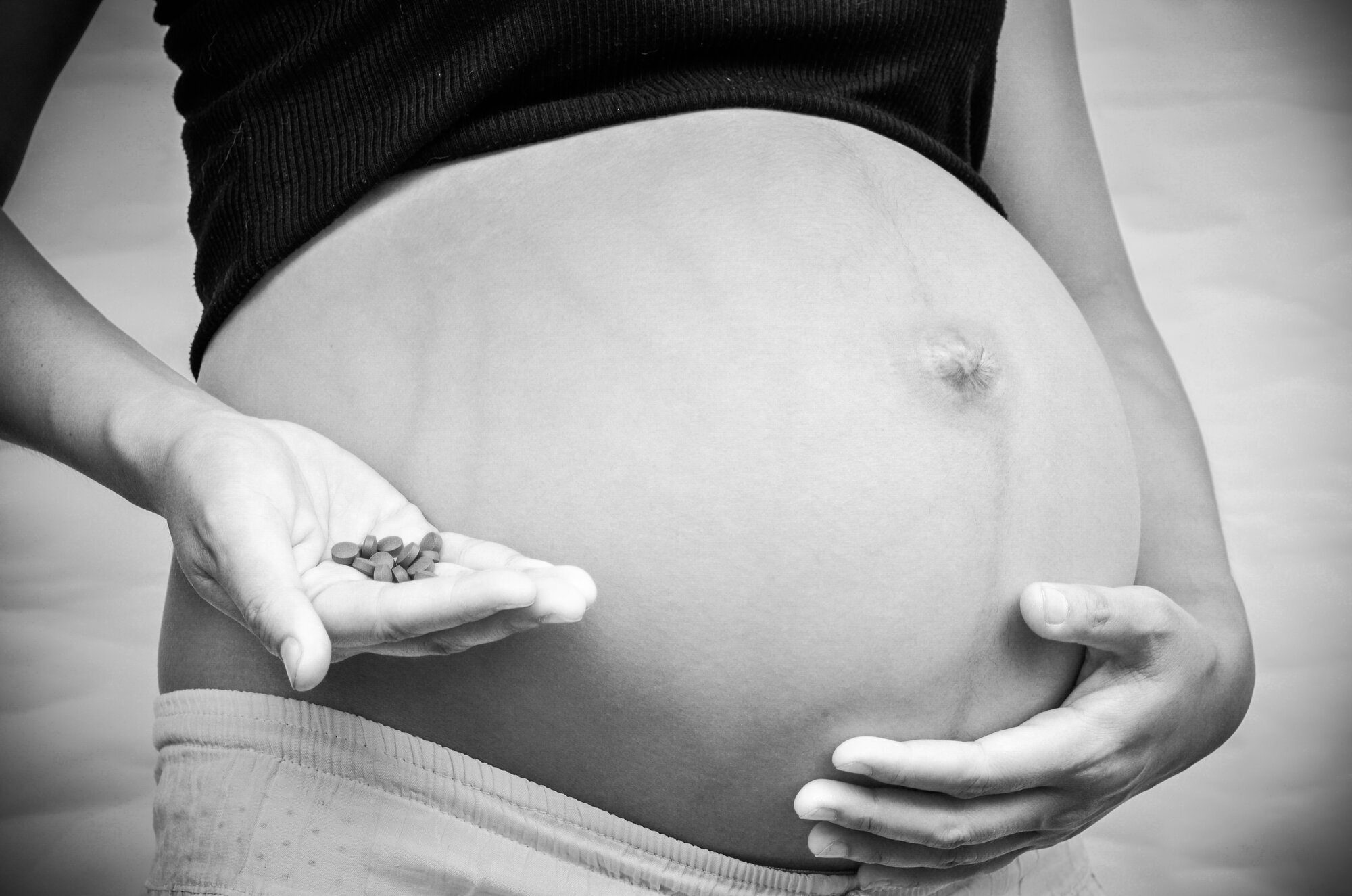 graviditet, legemidler Bildet viser en gravid mage og en hånd som holder mange piller.