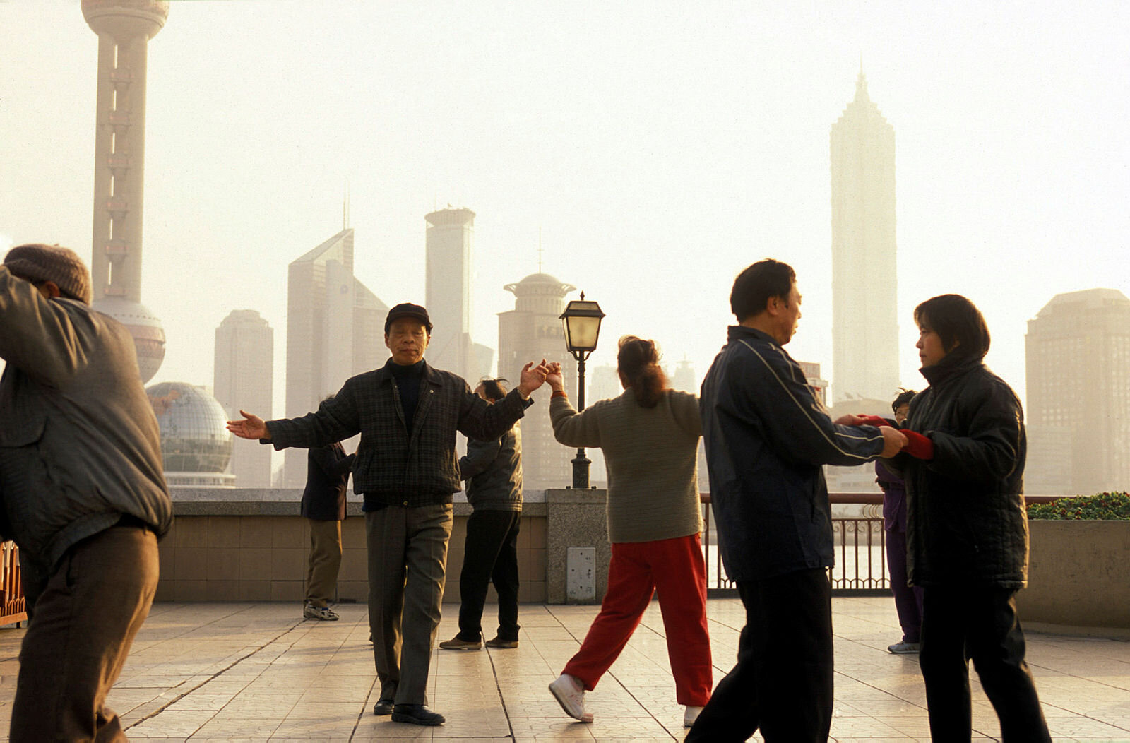 Morgengymnastikk Bildet viser en gruppe eldre mennesker i Shanghai som gjør en form for morgengymnastikk med byen i bakgrunnen.