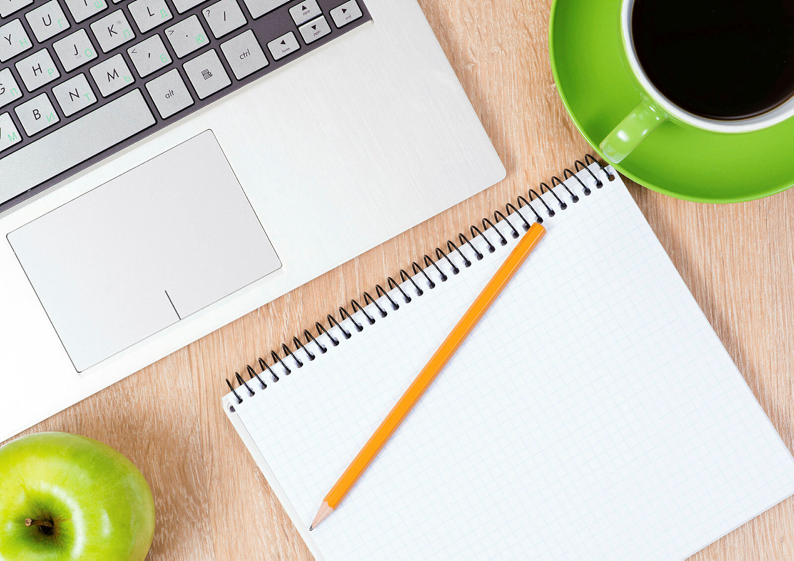 På kontorpulten Bildet viser deler av en bærbar PC, en skriveblokk, et eple og en kaffekopp.