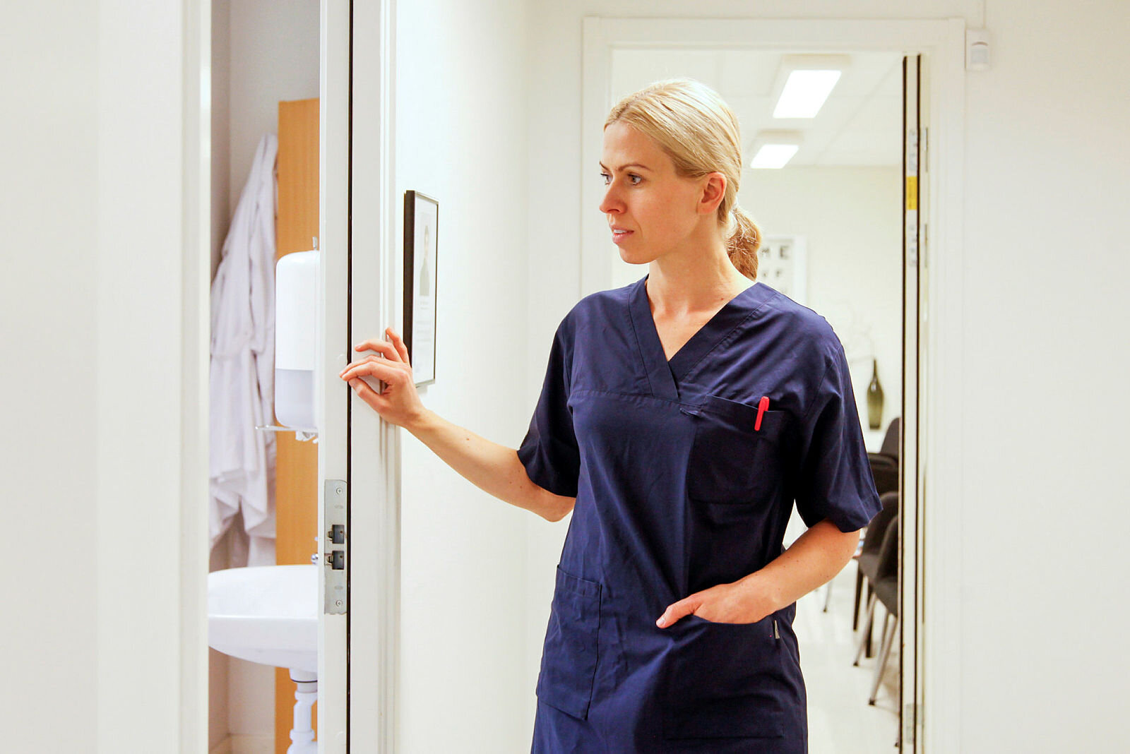 Sykepleier ser til pasientene Bildet viser en sykepleier som kikker inn døren til rommet pasienten er på
