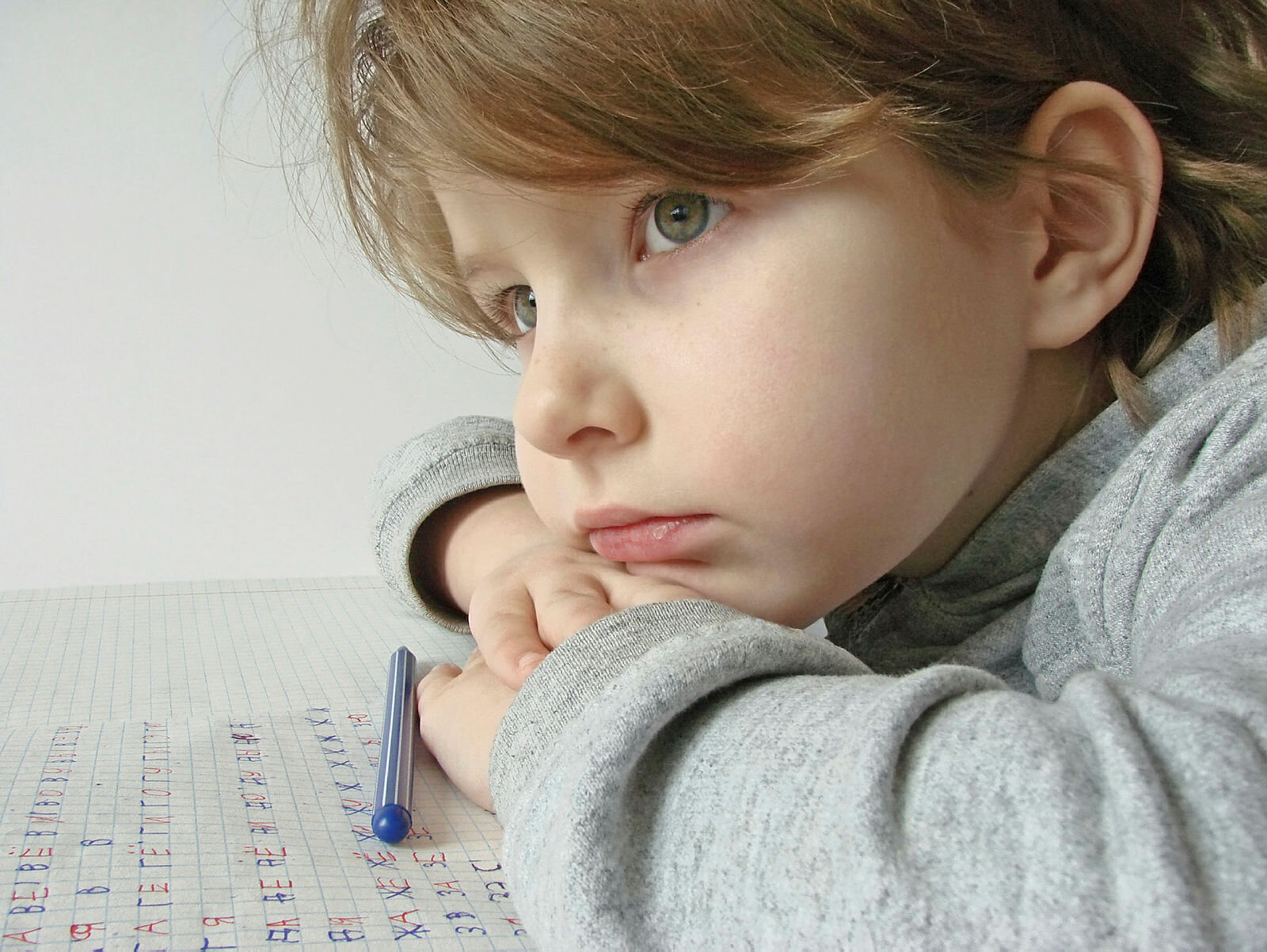Tankefull jente Bildet viser en tankefull jente som øver på å skrive bokstaver på et papir.