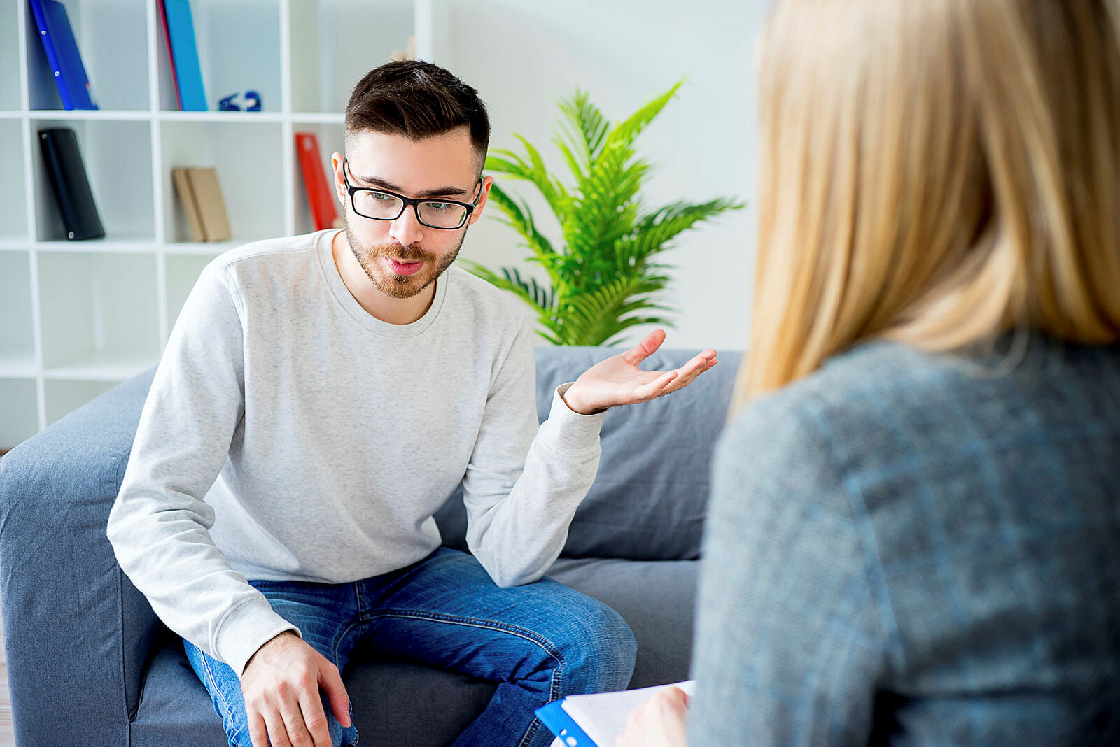 Ung mann hos terapeuten Bildet viser en ung mann som sitter i en sofa, tvers overfor en kvinnelig terapeut, som vi ser ryggen av.