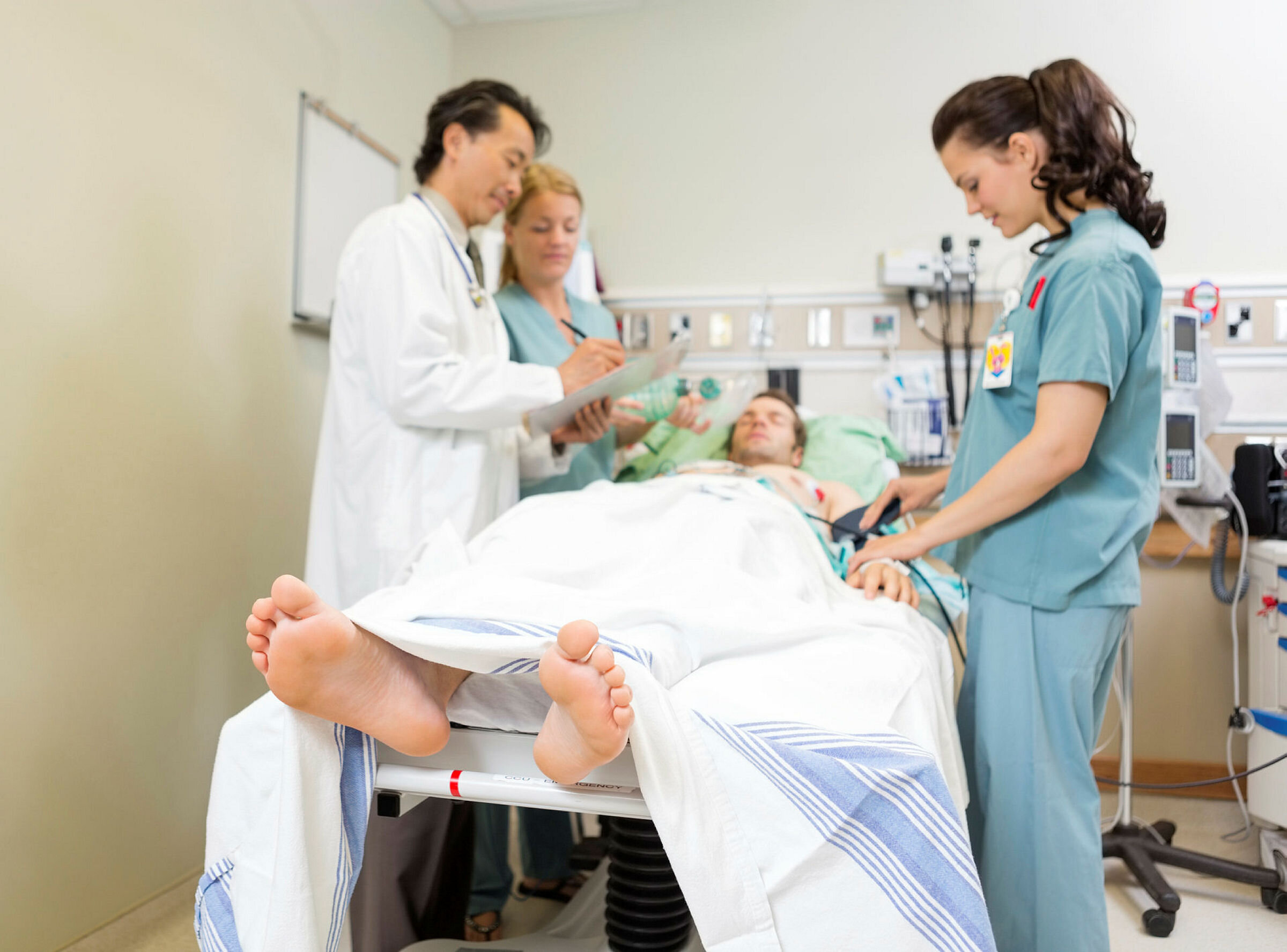 Bildet viser en pasient som ligger i en sykehusseng mens to sykepleiere og en lege står ved siden av. Legen skriver på et skjema.