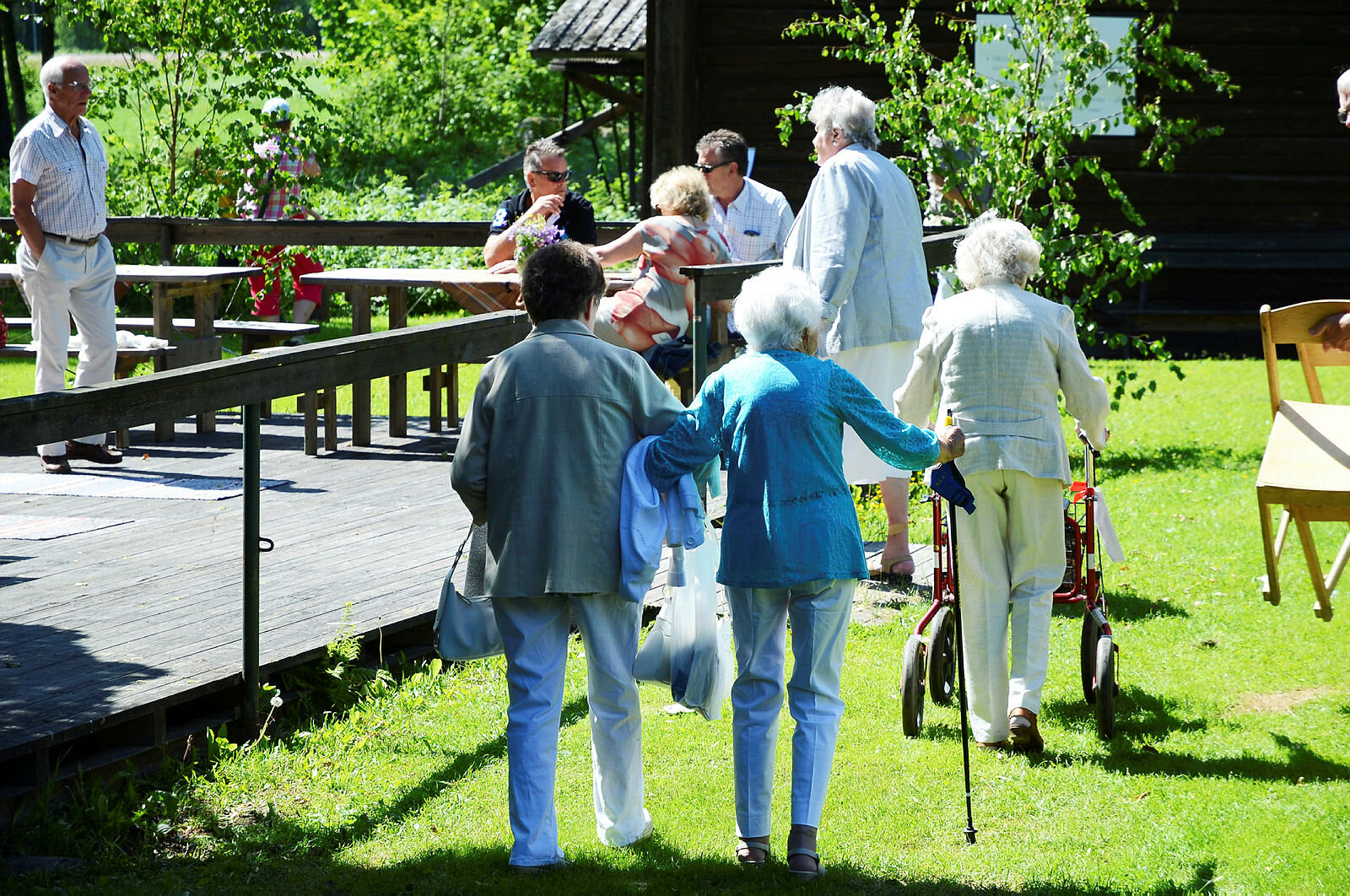 Eldre personer som går over en gressplen på vei til et arrangement. Noen har rullator.