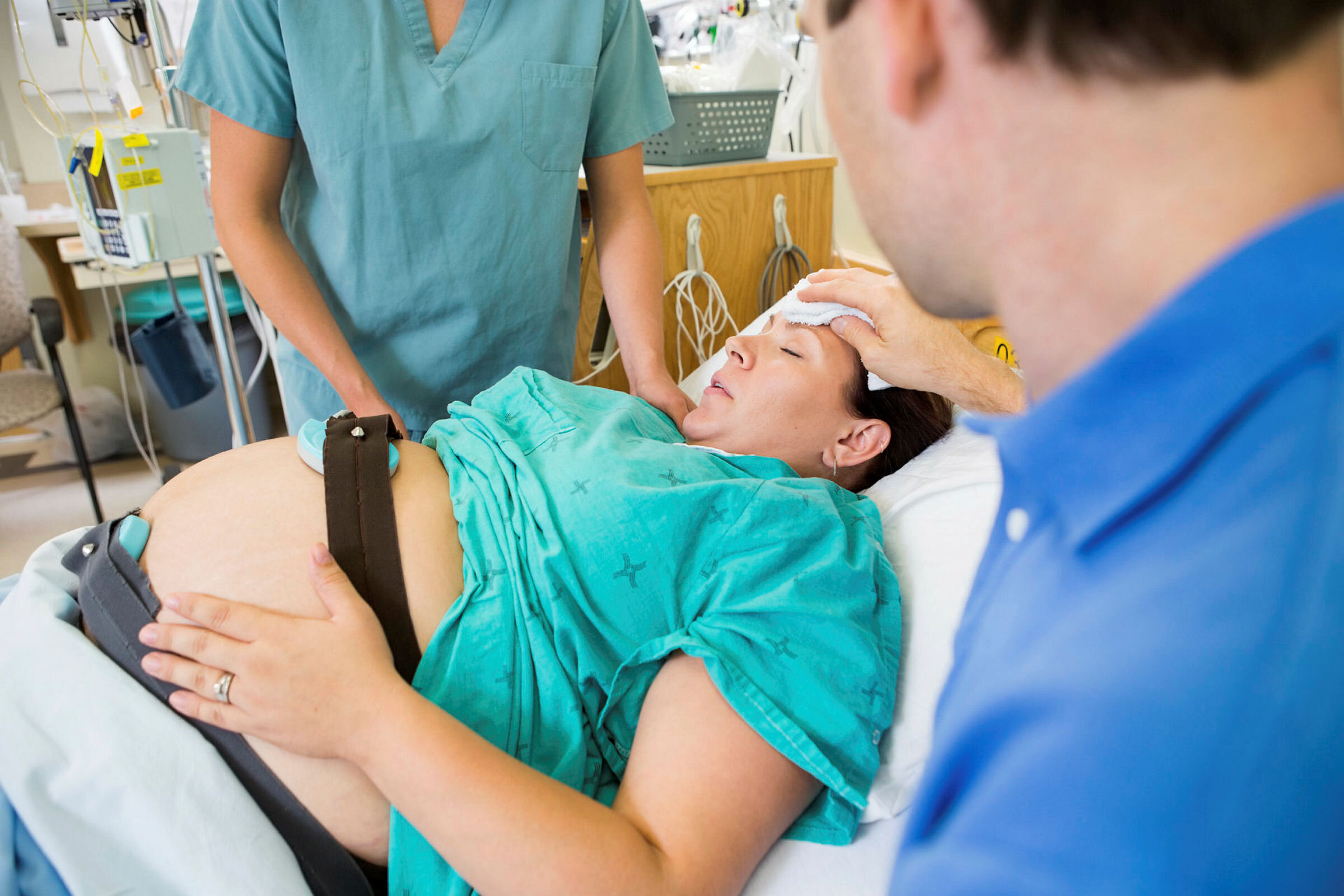 Kvinne som føder Bildet viser en kvinne som holder på å føde. Sykepleierne og legen måler fosterlyden, mens faren tørker pannen til kvinnen.