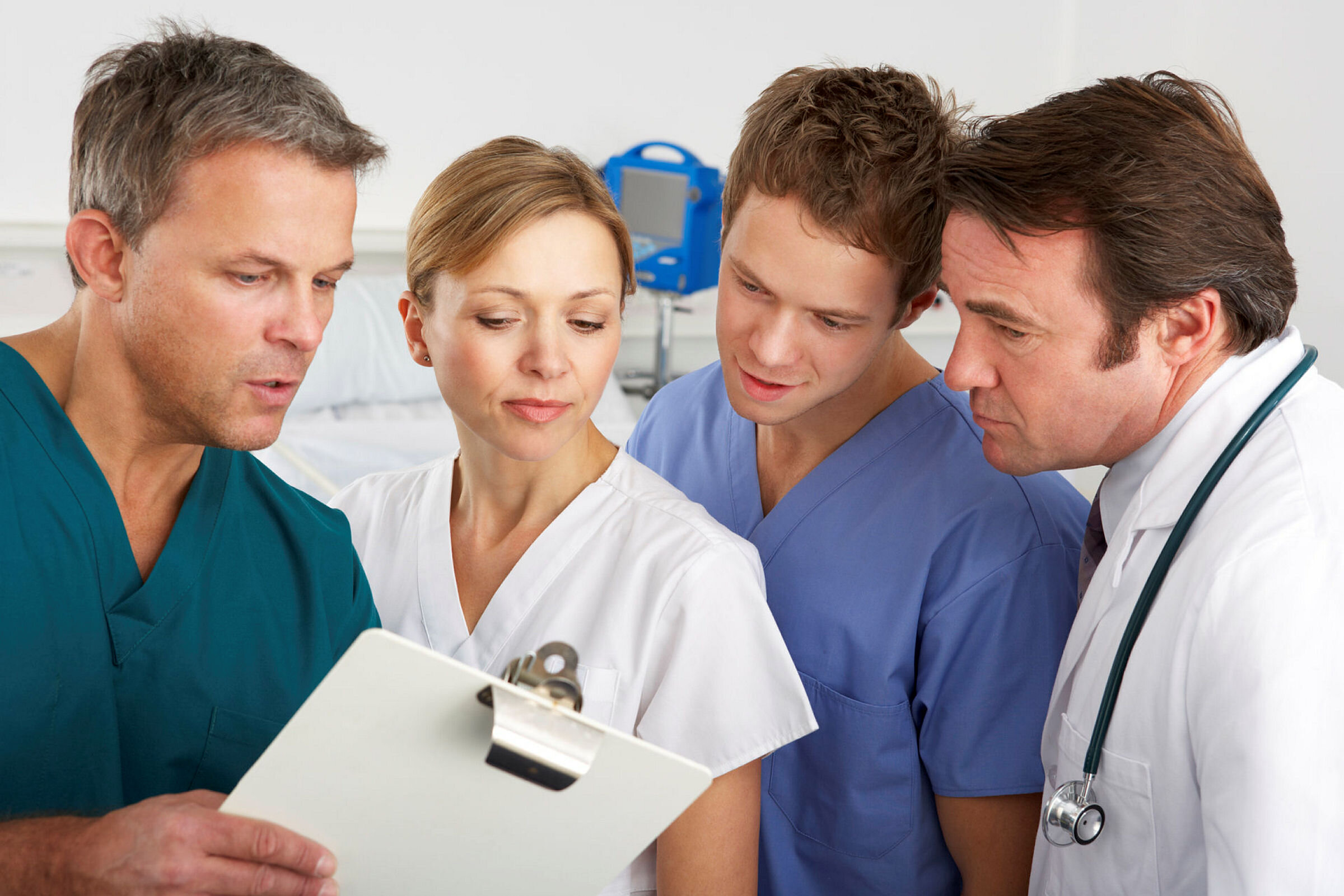 Bildet viser sykepleiere og leger som står og snakker sammen over en clipboard. Det er både menn og kvinner blant de fire.