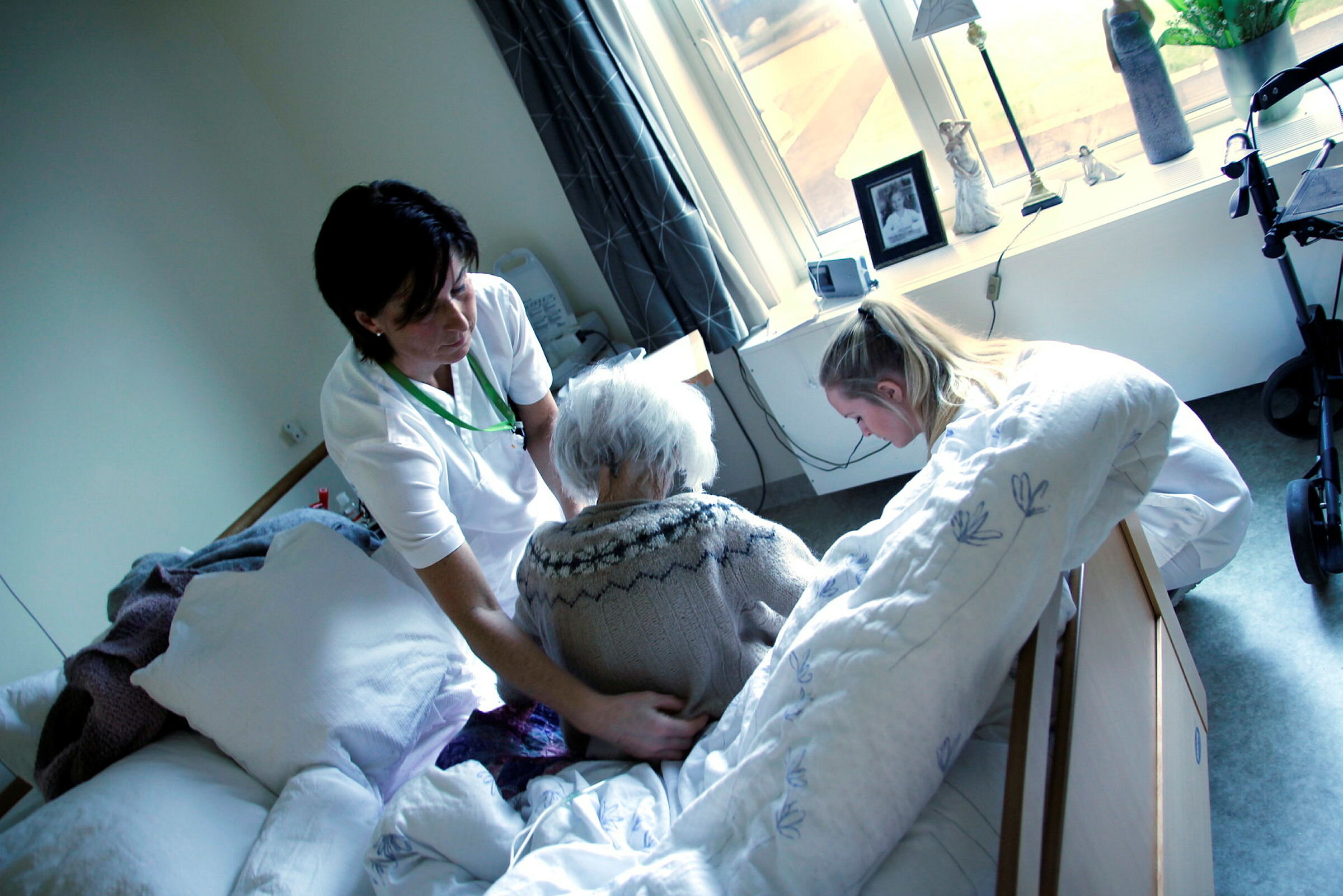 Pasientomsorg på sykehjem. Bildet viser to sykepleiere som hjelper en pasient i sengen hennes på Karmøy sykehjem.