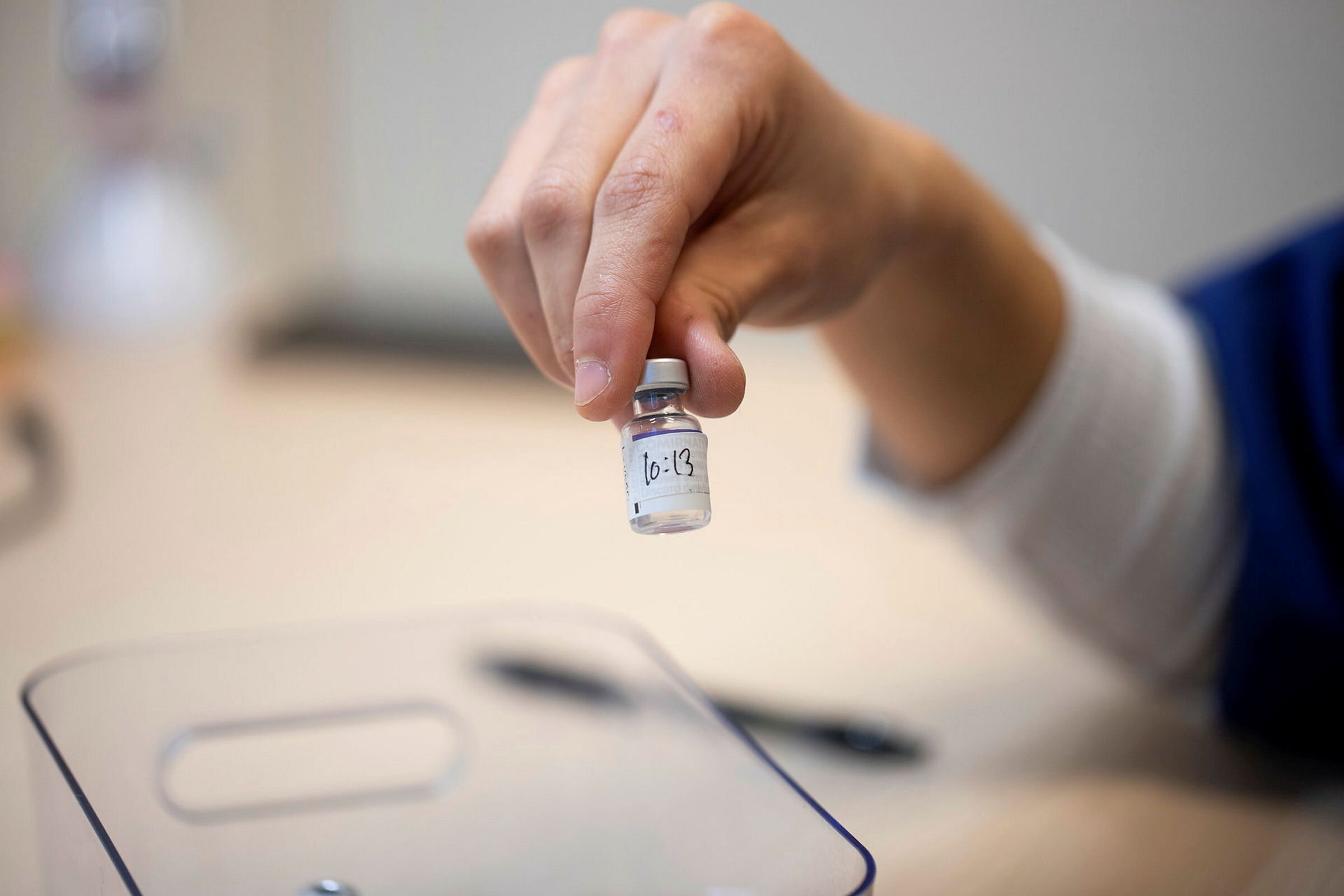 Bildet viser en hånd som holder opp en flaske med koronavaksine Bildet viser en hånd som holder opp en flaske med koronavaksine