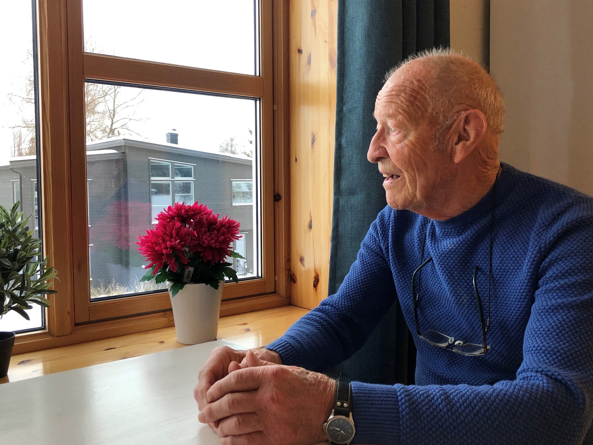 Eldre mann i blå genser ser ut av vindu.